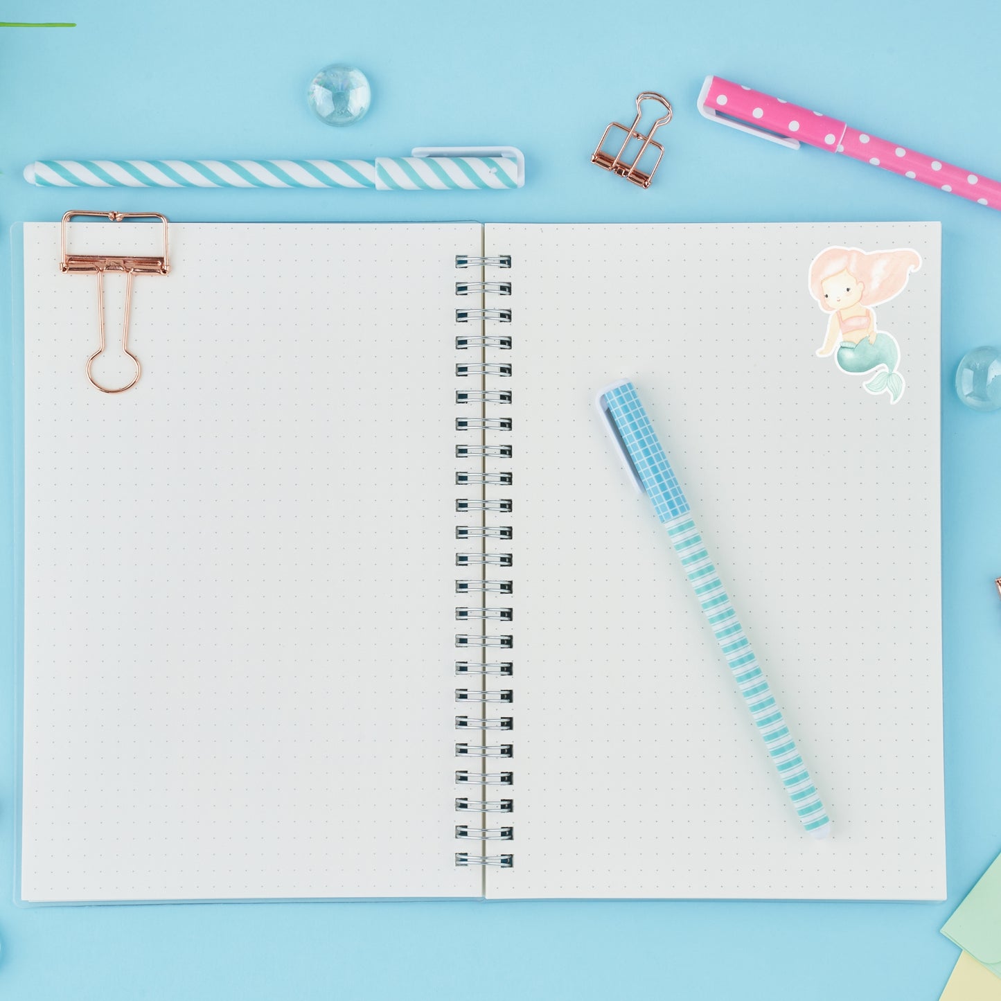 Sticker Meerjungfrau rosa auf einem Notizbuch mit Stift und Büroklammern, handgefertigt in zarten Pastelltönen, ideal für Bullet Journals und Dekorationen.