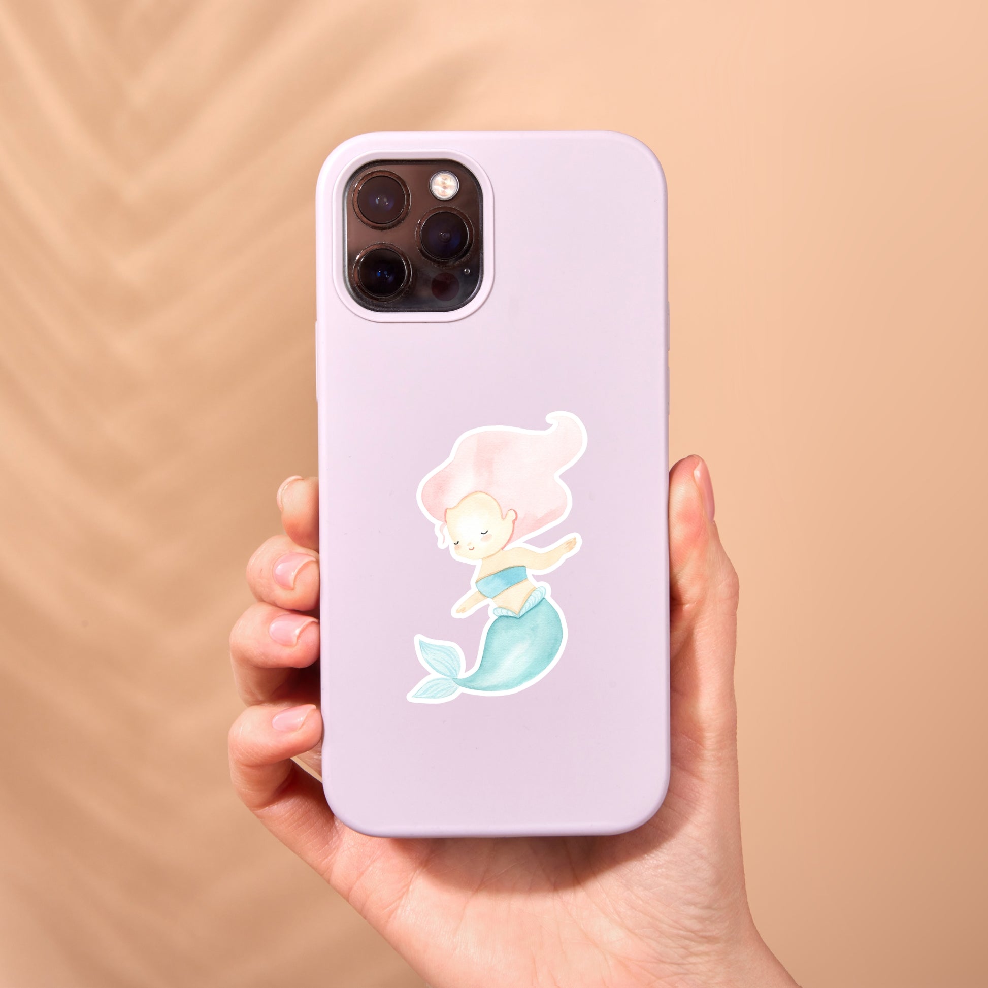 Eine Hand hält eine Handyhülle mit einem Sticker Meerjungfrau pink, der eine handgezeichnete Meerjungfrau in Pastelltönen zeigt.