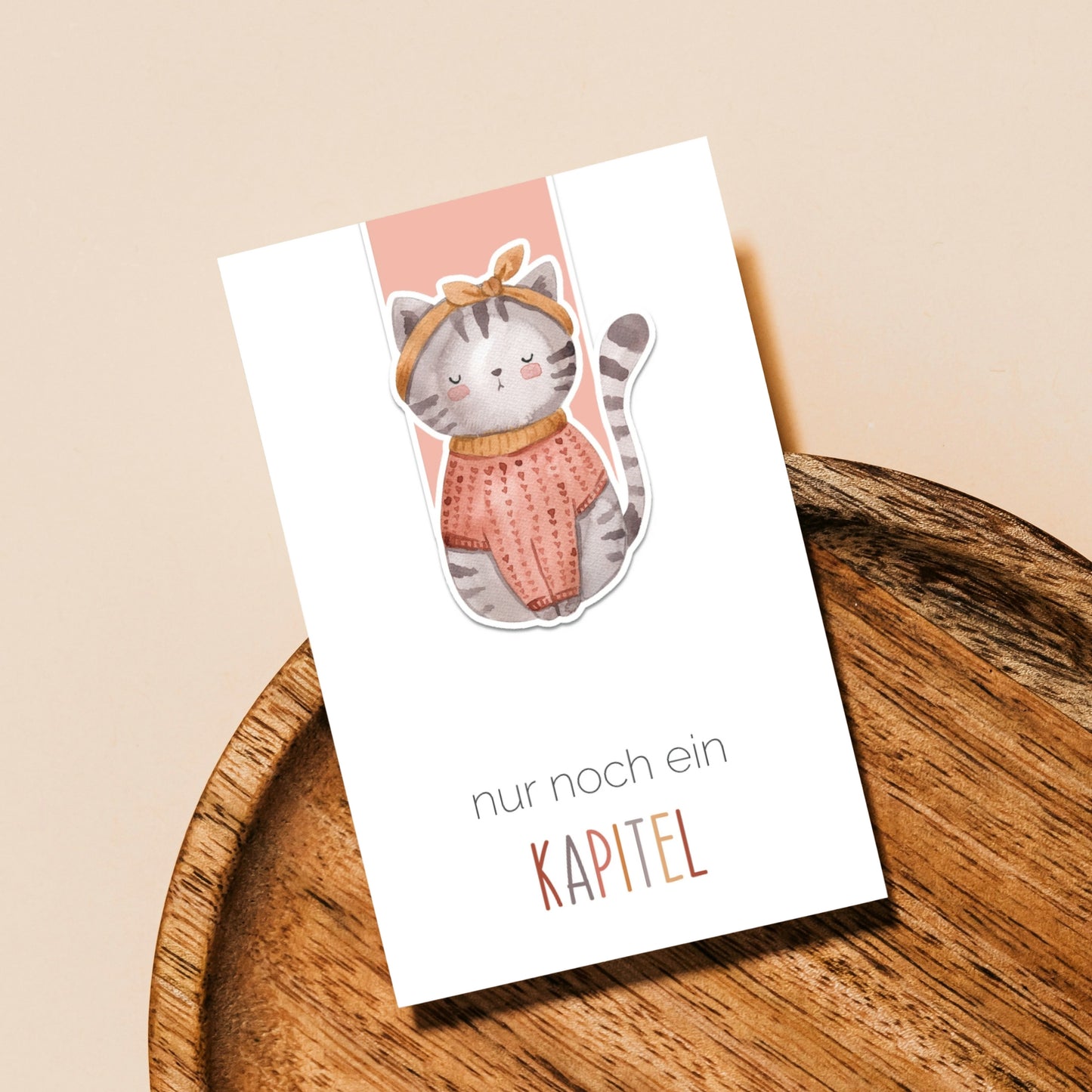 Magnetisches Lesezeichen Katze auf einem Holztablett, zeigt eine Katze in Pullover und Schleife, ideal für Buchliebhaber und handgemacht auf hochwertigem Papier.