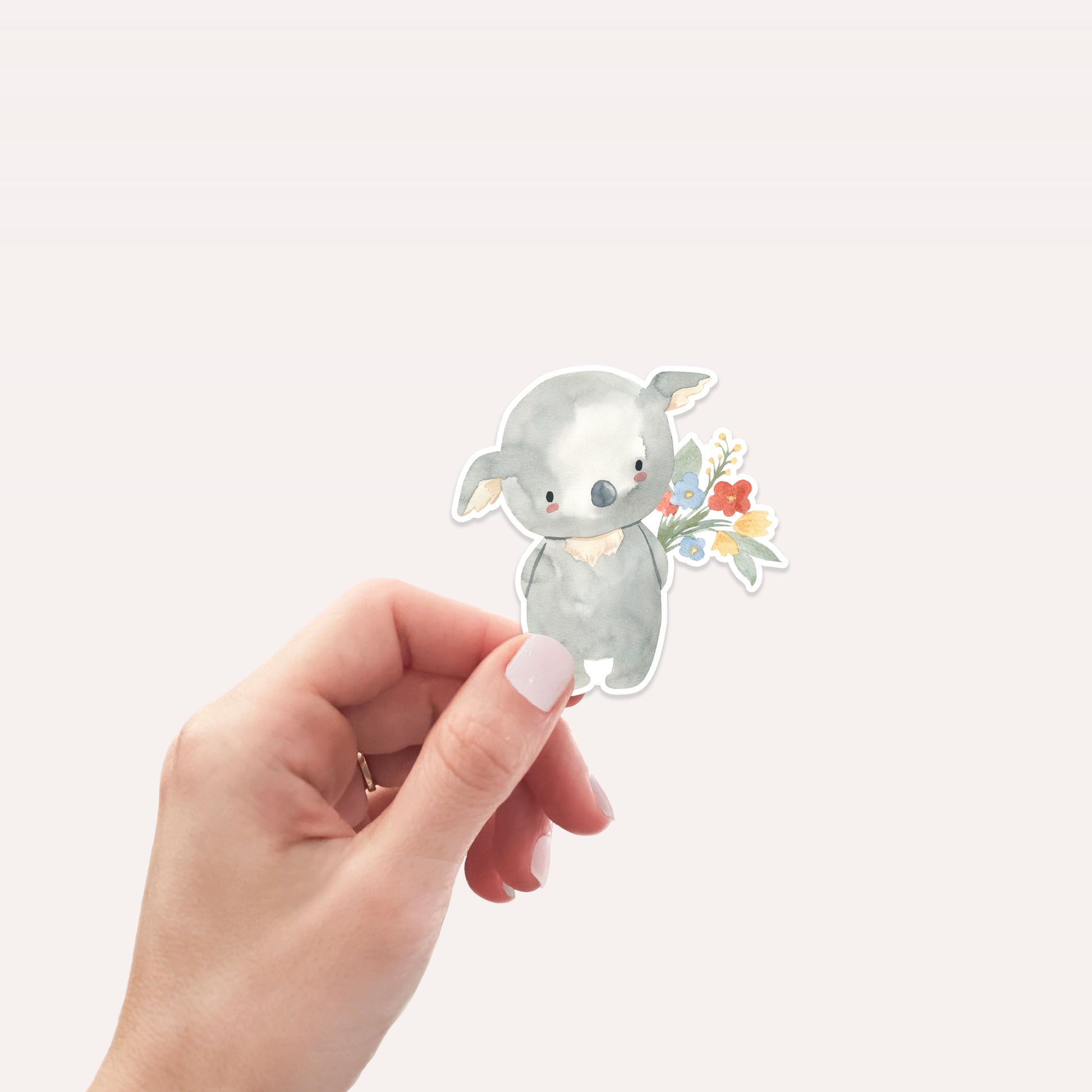 Hand hält den Sticker Koala & Blumen: Ein handgemalter Vinyl-Aufkleber mit Koala und Blumenstrauß, ideal für Bullet Journals, Laptops oder als Geschenk.