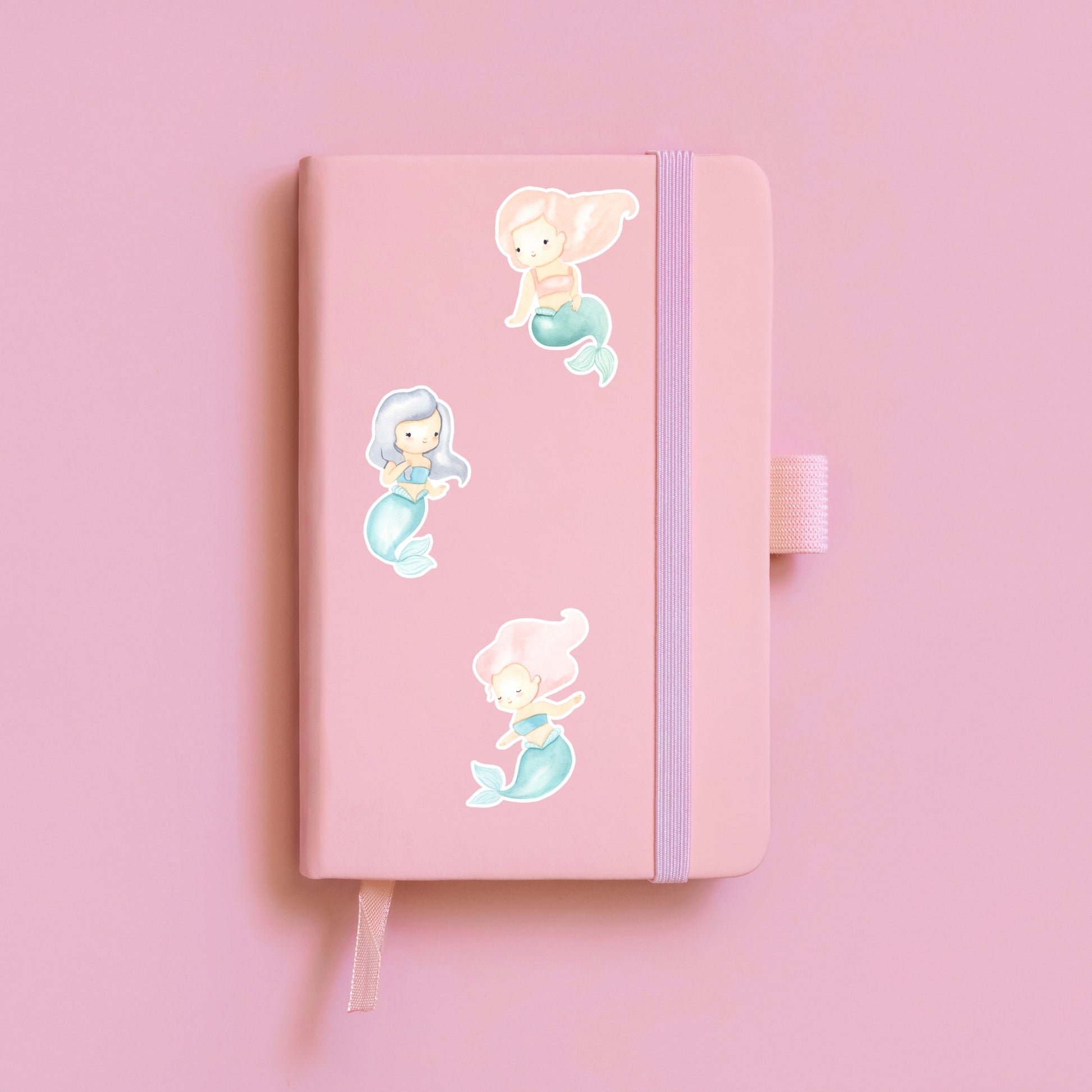 Sticker Meerjungfrau pink: Ein pinkes Notizbuch mit handgemaltem Meerjungfrau-Sticker in zarten Pastelltönen, ideal für Bullet Journals oder Schulhefte.