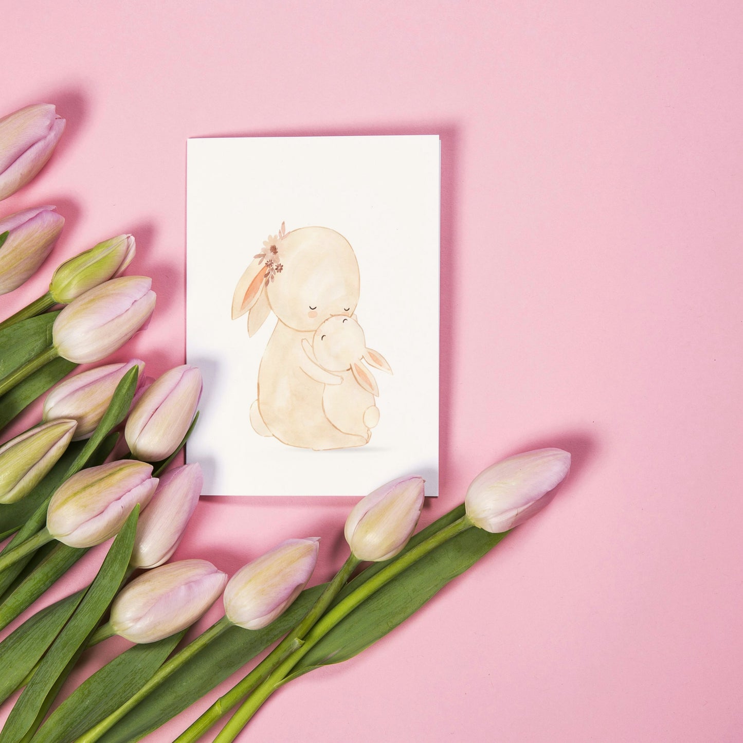Karte Mama Hase & Baby A6, zeigt Aquarellzeichnung von zwei umarmenden Hasen, umgeben von rosa Tulpen. Ideal für Geburtstags- oder Muttertagsgrüße.