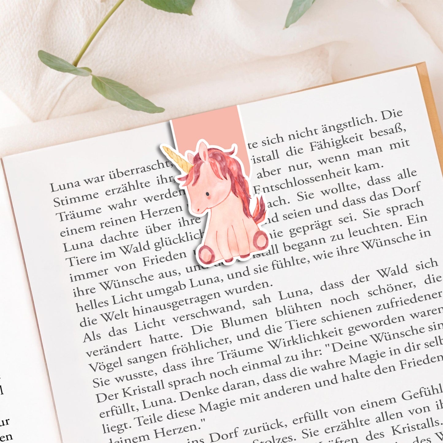 Magnetisches Lesezeichen Einhorn, handgemalt, 6x3,5 cm, mit schützender Vinylschicht und Magneten innen, ideal für Buchliebhaber als Geschenk. Auf Buchseite präsentiert.