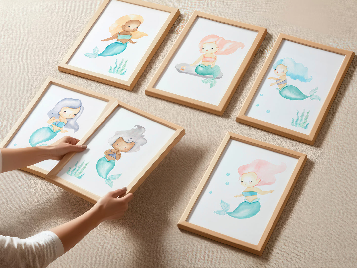 Sechs Holzrahmen mit Meerjungfrauen-Illustrationen, jede in anderer Pose und Haarfarbe, auf neutralem Untergrund. Hände justieren einen Rahmen. Posterset Meerjungfrauen A3 & A4.