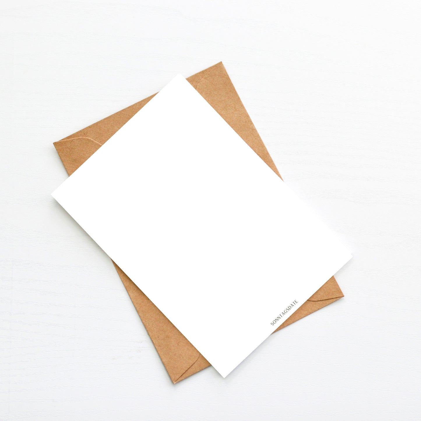 Karte Regenbogen mit Herz A6 auf weißem Holzuntergrund, mit beiliegendem braunem Umschlag. Karte unbedruckt sichtbar; Rückseite beschrift- und bestempelbar.