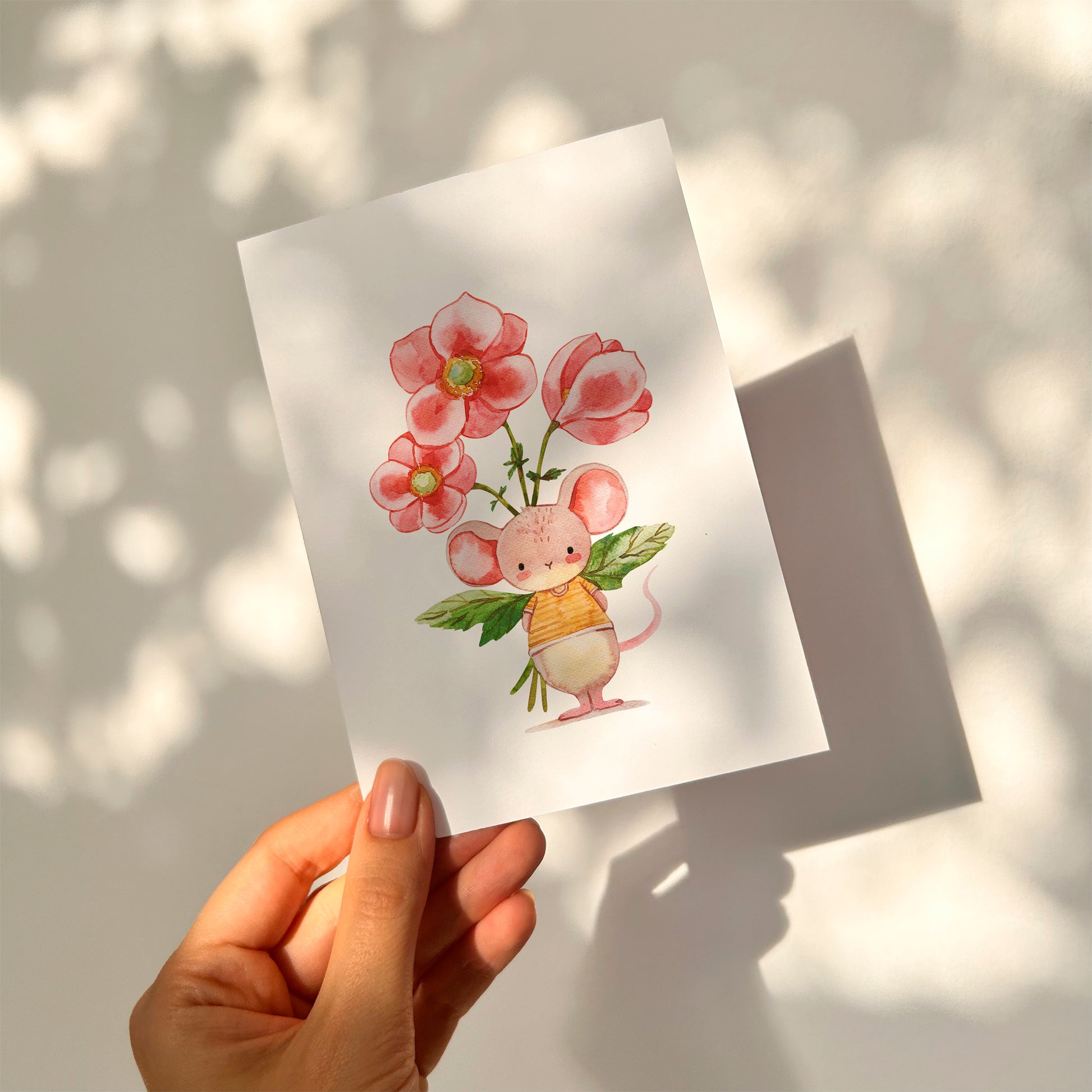 Postkarte Karte Maus mit Blumenstrauß A6, zeigt eine Hand, die eine Karte mit einem Cartoon-Mausmotiv und Blumenstrauß hält, auf hochwertigem, beschreibbarem Naturpapier.