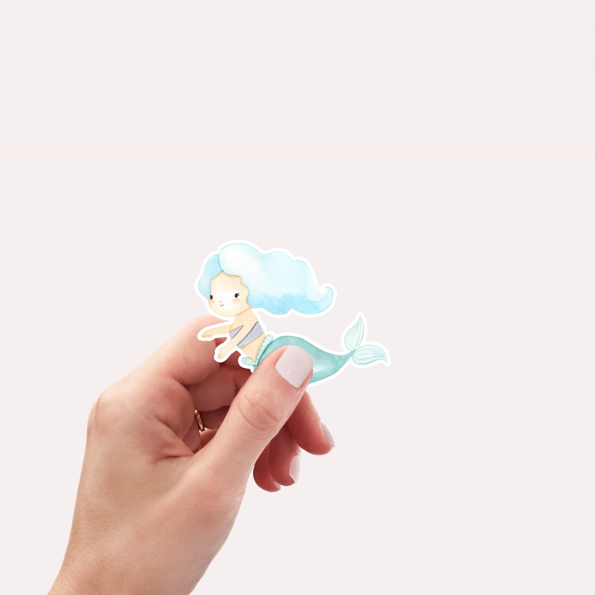 Hand hält Sticker Meerjungfrau blau, cartoonhaft, auf hochwertigem Vinyl. Ideal für Bullet Journals, Laptops oder als Bastelzubehör. Spritzfest und langlebig.