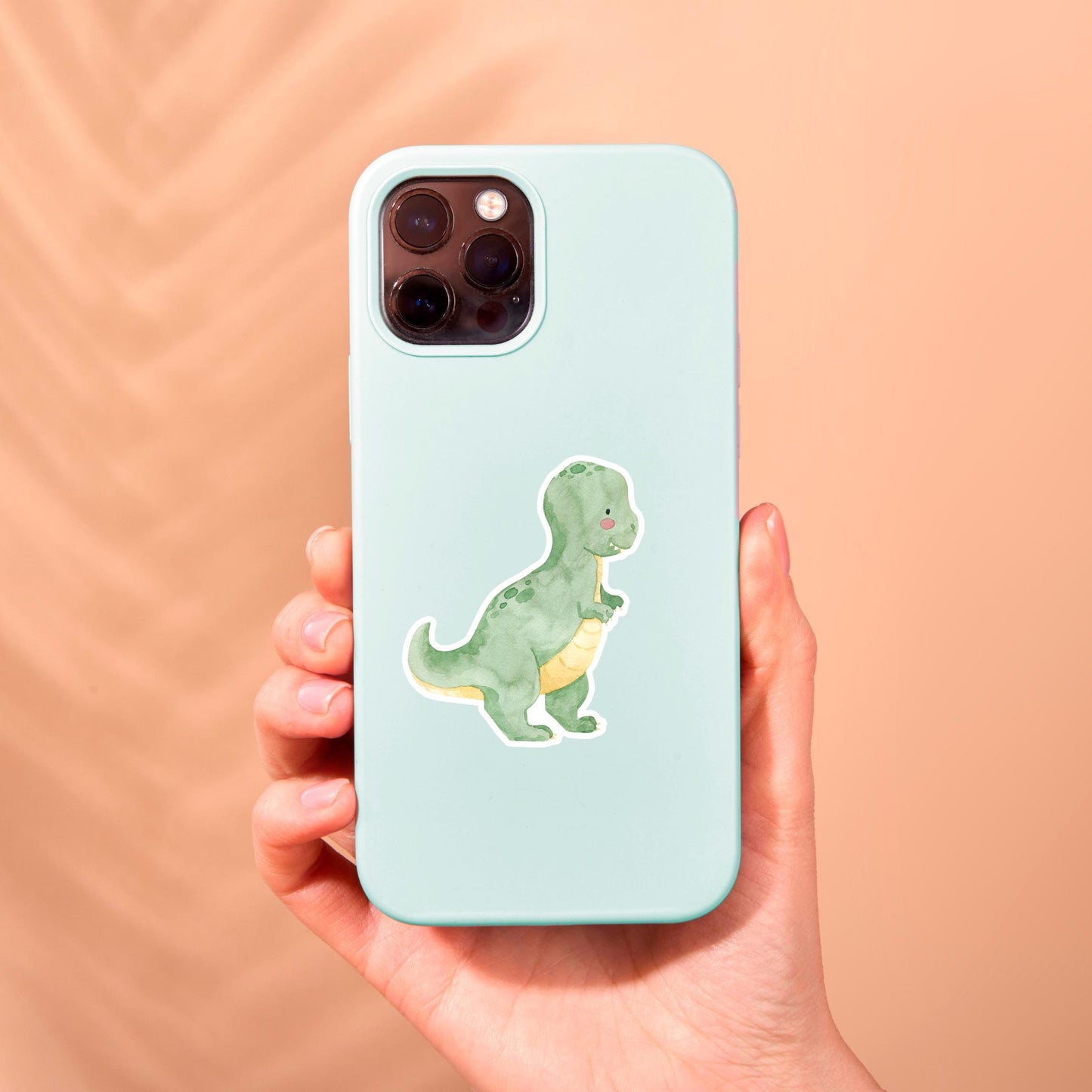 Hand hält eine Handyhülle mit Sticker Dinosaurier Tyranno, handgefertigter Vinyl-Sticker, spritzfest und langlebig, ideal für Dino-Fans zur individuellen Gestaltung.