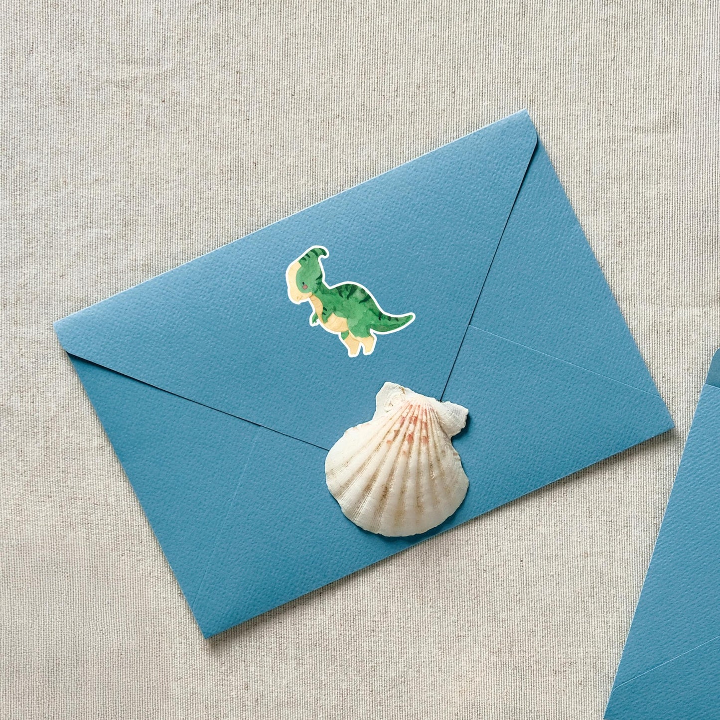 Sticker Dinosaurier Parasauro: Ein blauer Umschlag mit einem handgemalten Dinosaurier-Vinyl-Sticker und einer Muschel, ideal zur Dekoration von Notebooks oder Einladungen.