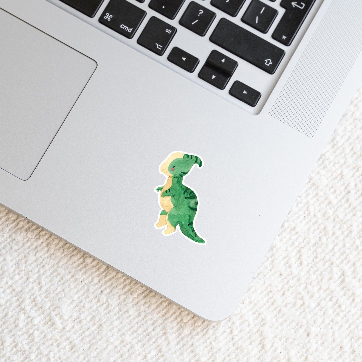 Laptop mit Sticker Dinosaurier Parasauro, ein handgemalter Dino-Aufkleber aus hochwertigem Vinyl, ideal für Bullet Journals und mehr. Sichtbar: Tastatur und Cartoon-Dinosaurier.