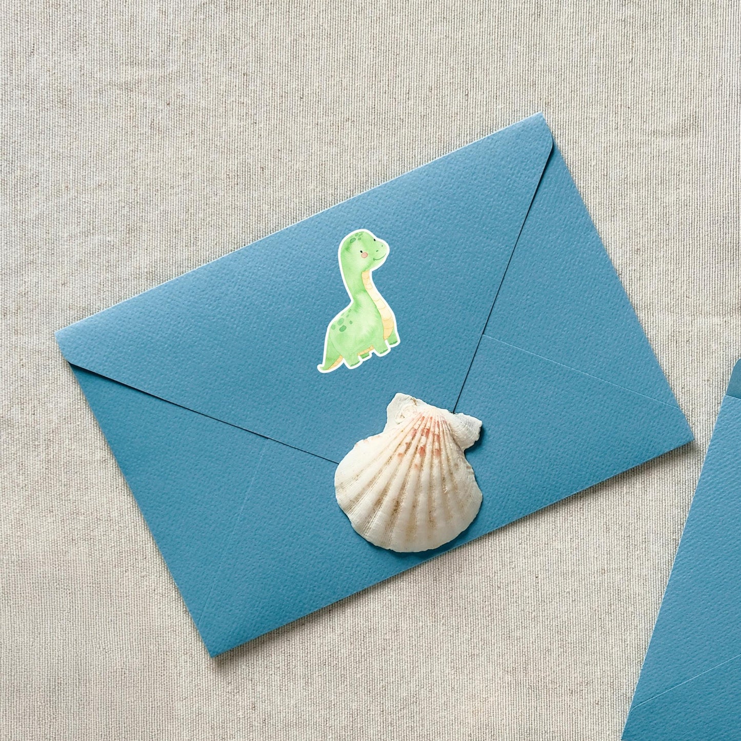 Sticker Dinosaurier hellgrün auf blauem Umschlag mit Muschel. Handgefertigter, spritzfester Vinyl-Sticker, ideal für Bullet Journals, Schulhefte und kreative Dekorationen.