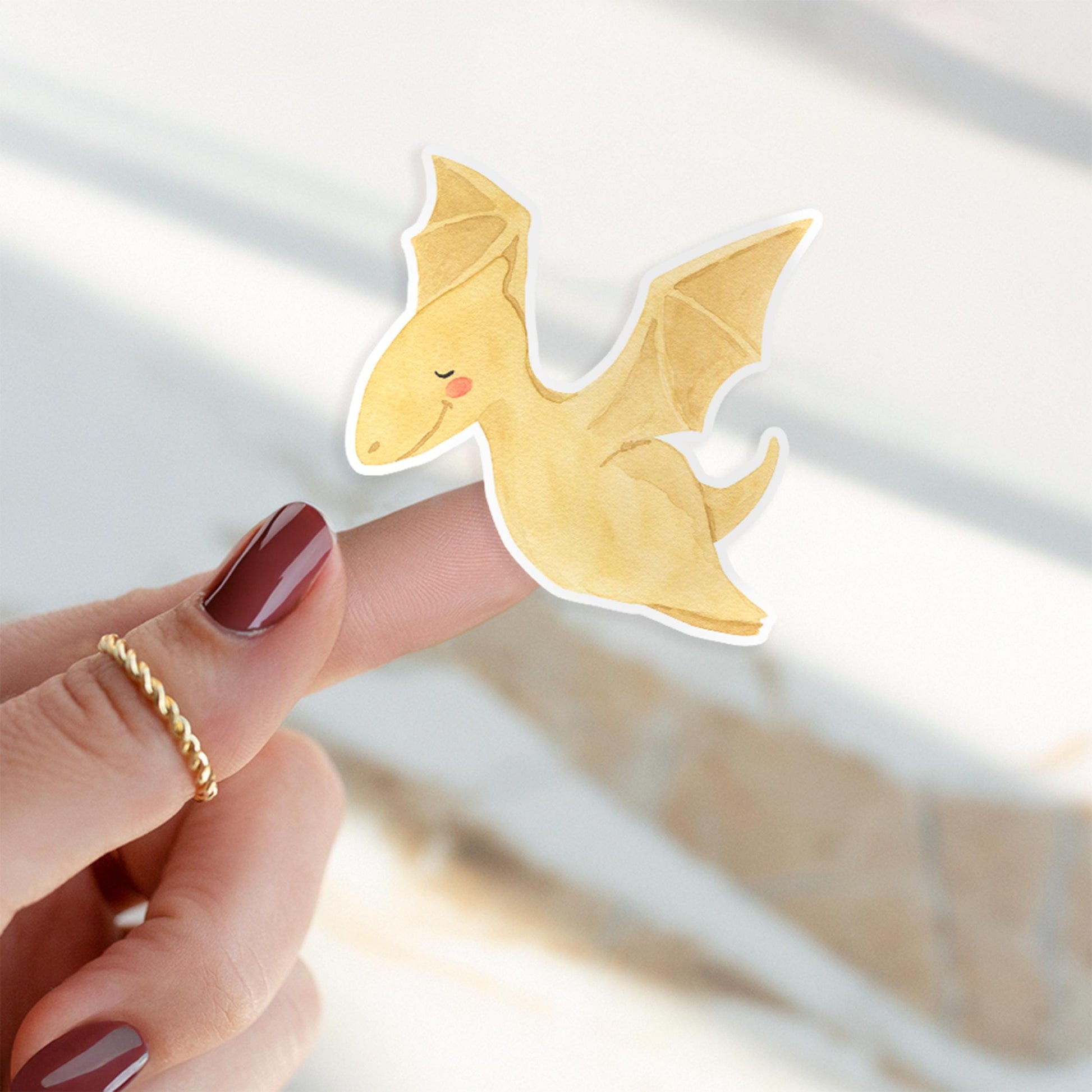 Sticker Dinosaurier fliegt: Ein gelber Dino-Sticker ruht auf einem Finger. Handgefertigt aus Vinyl, ideal für kreative Projekte und Dekorationen.