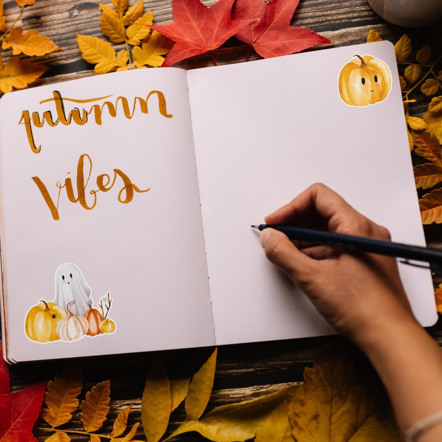 Sticker Halloween: Eine Hand schreibt in ein Notizbuch, umgeben von herbstlichen Blättern und Kürbissen, passend zur handgefertigten Spooky-Season-Sticker-Thematik.