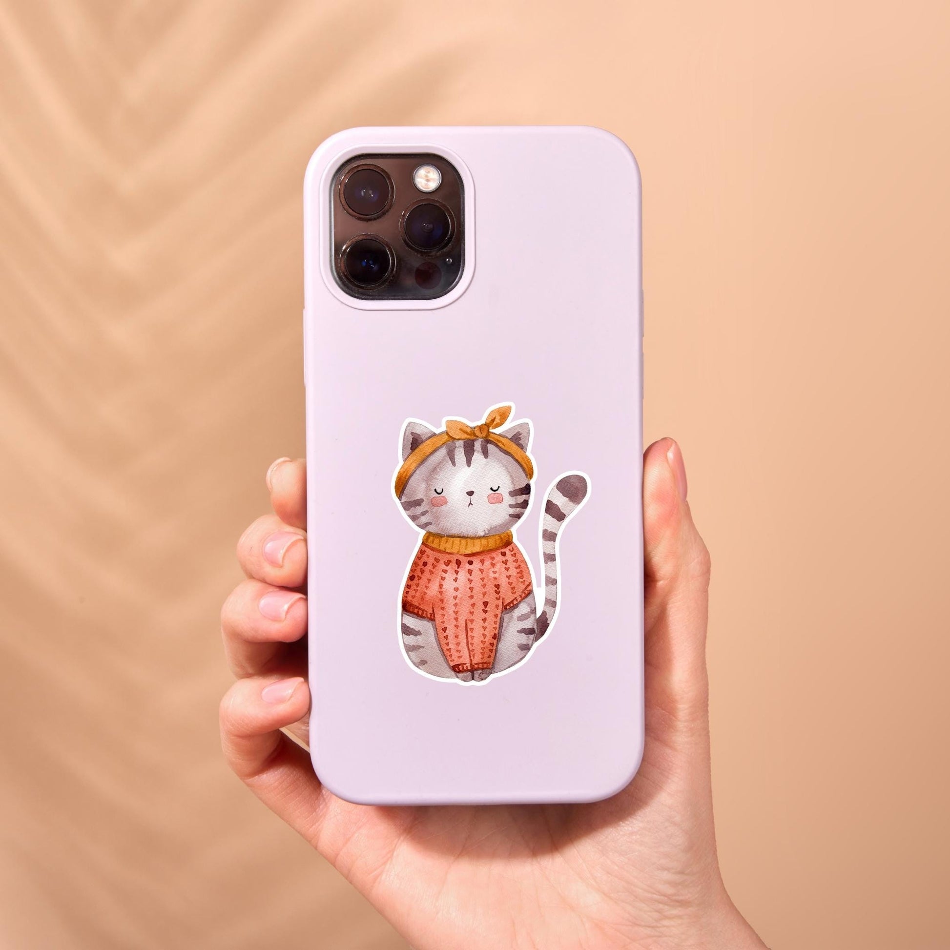 Sticker Katze: Eine Hand hält eine Handyhülle mit einem Cartoon einer Katze im Vintage-Stil, die einen Pullover trägt. Perfekt für Katzenliebhaber.