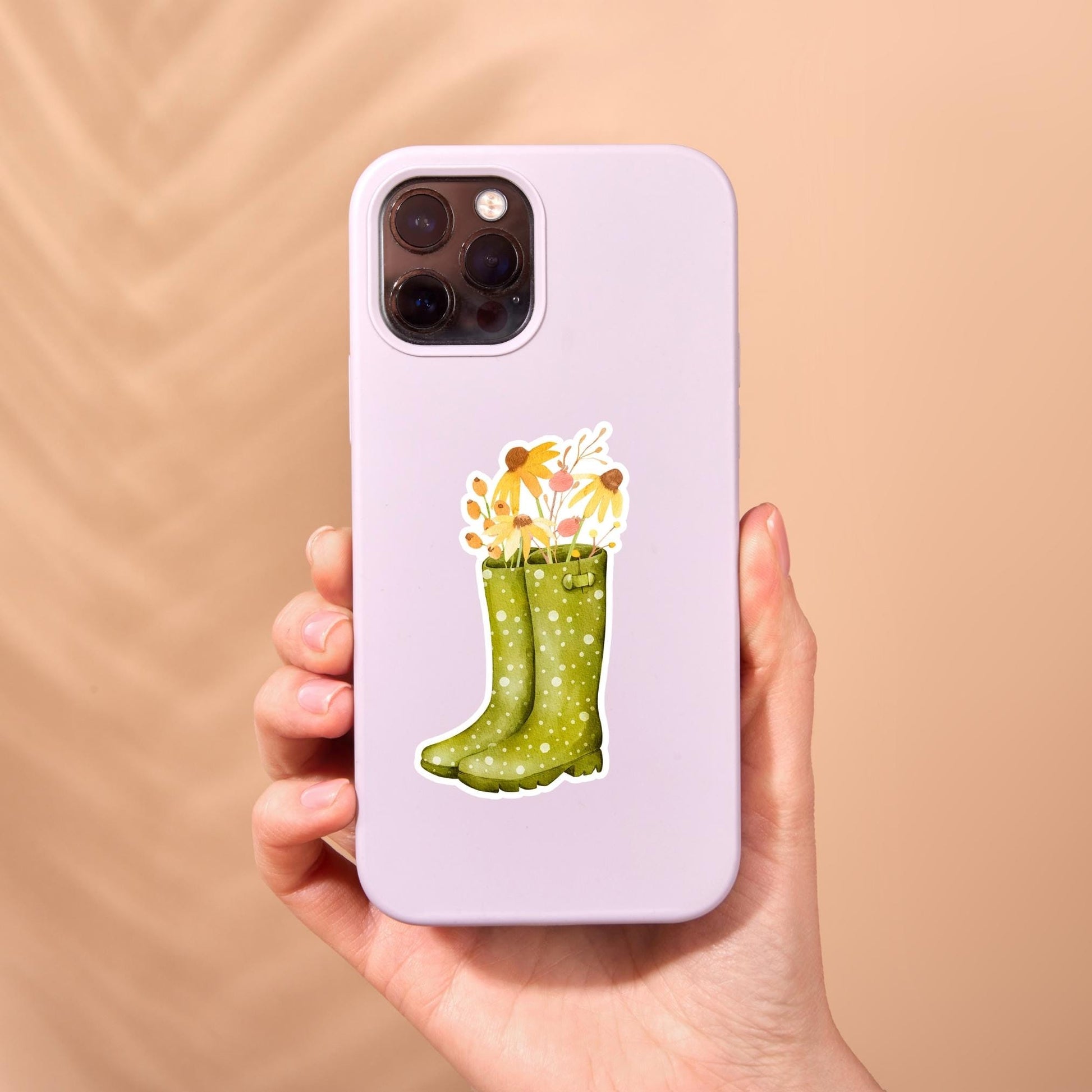 Hand hält eine Handyhülle mit Sticker Herbstblumen, zeigt grünen Gummistiefel und gelbe Blumen, inspiriert von hochwertigem, spritzfestem Vinyl-Aufkleber.