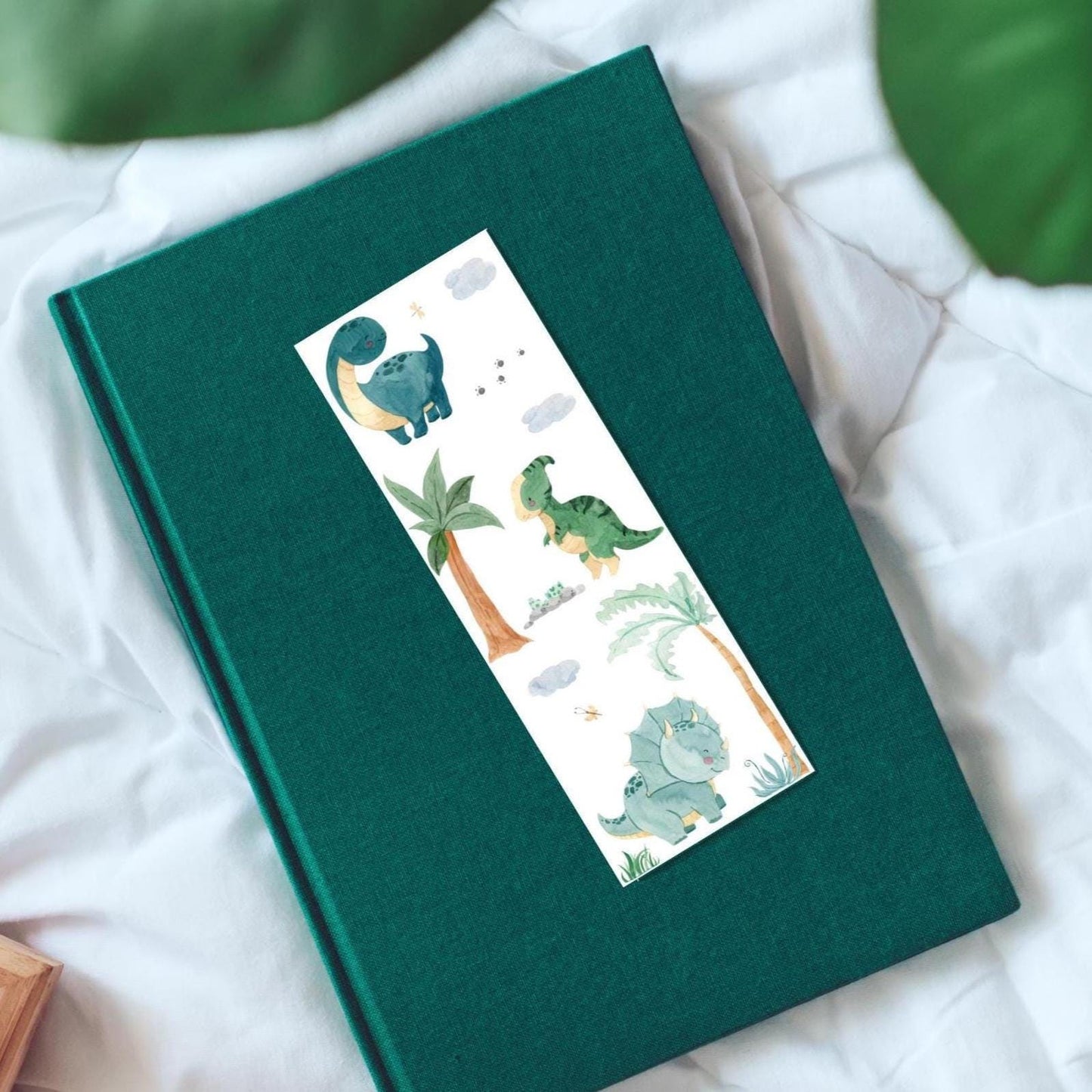 Lesezeichen Dinosaurier 2er Set auf einem Buch mit einem handgemalten, beidseitig bedruckten Dinosaurier-Motiv, ideal für Bücherfreunde und als Geschenk.