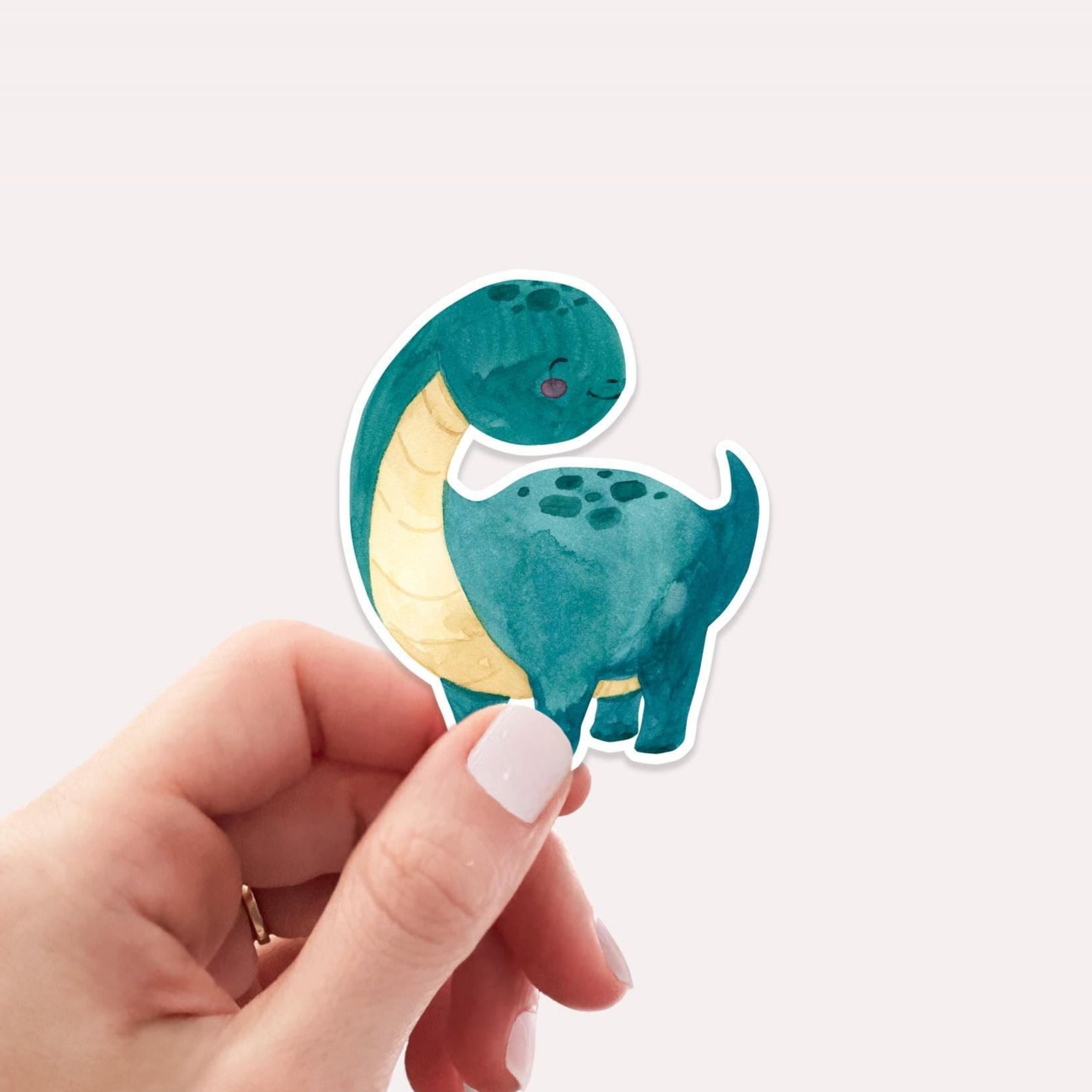 Ein Hand hält den Sticker Dinosaurier dunkelgrün, einen handgemalten Vinyl-Aufkleber in Dinosaurierform, ideal für kreative Dekorationen auf Notizbüchern oder Laptops.
