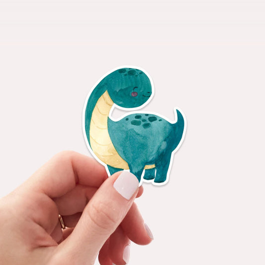 Ein Hand hält den Sticker Dinosaurier dunkelgrün, einen handgemalten Vinyl-Aufkleber in Dinosaurierform, ideal für kreative Dekorationen auf Notizbüchern oder Laptops.