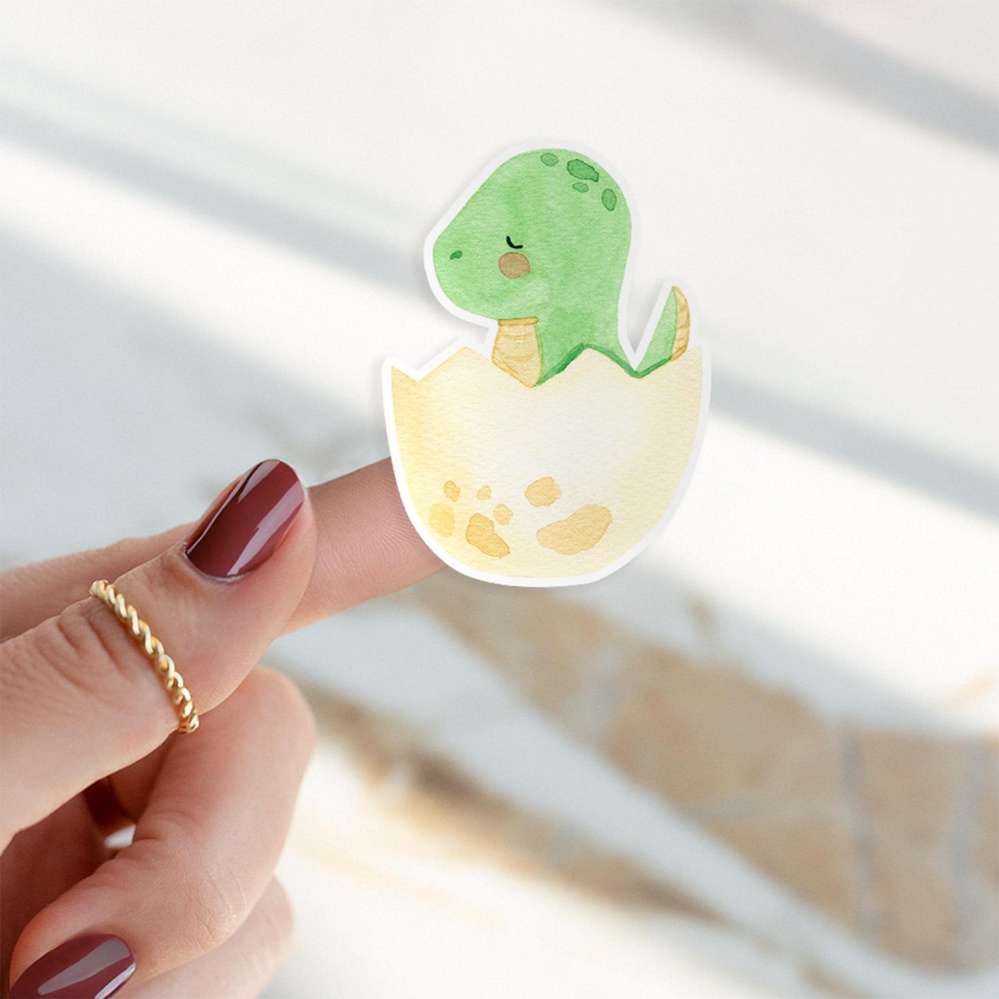 Ein Finger hält den Sticker Dinosaurier im Ei, ein detailreicher, langlebiger Vinyl-Aufkleber ideal für kreative Projekte und individuelle Designs.