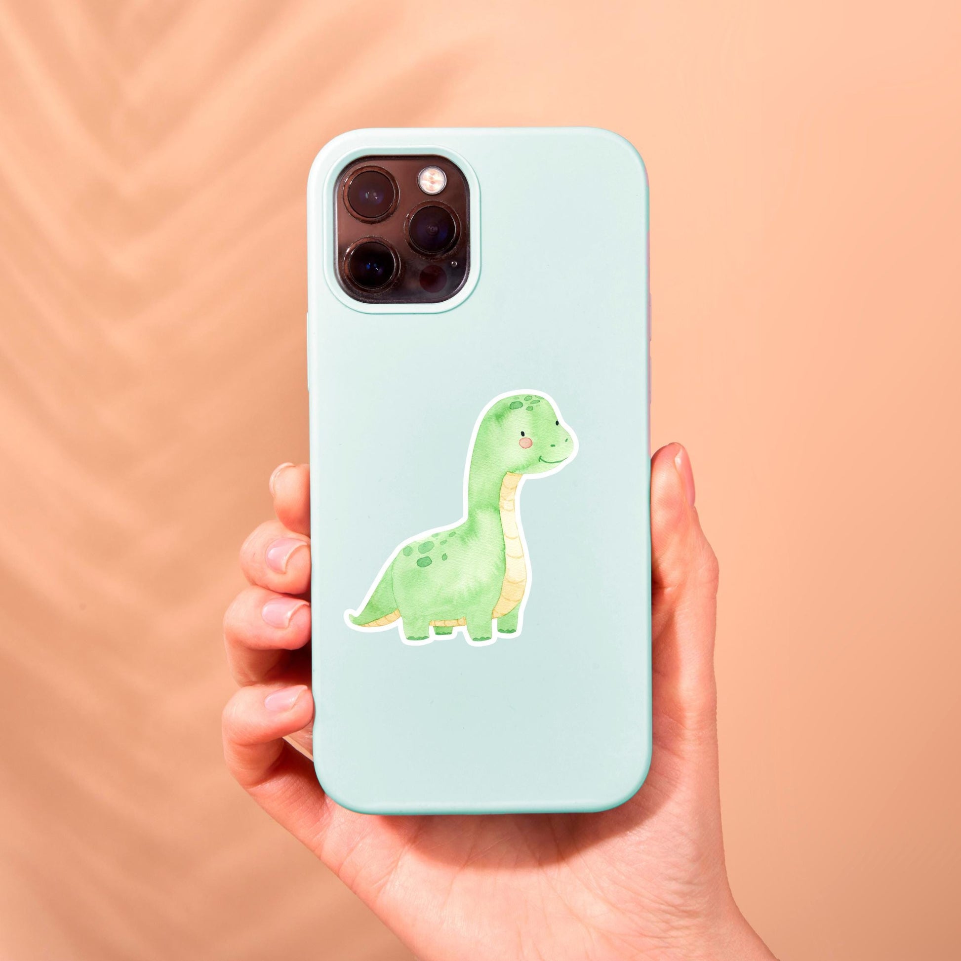 Hand hält Handyhülle mit Sticker Dinosaurier hellgrün, einem handgemalten, spritzfesten Vinyl-Aufkleber. Perfekt für individuelle Gestaltung von Bullet Journals und mehr.