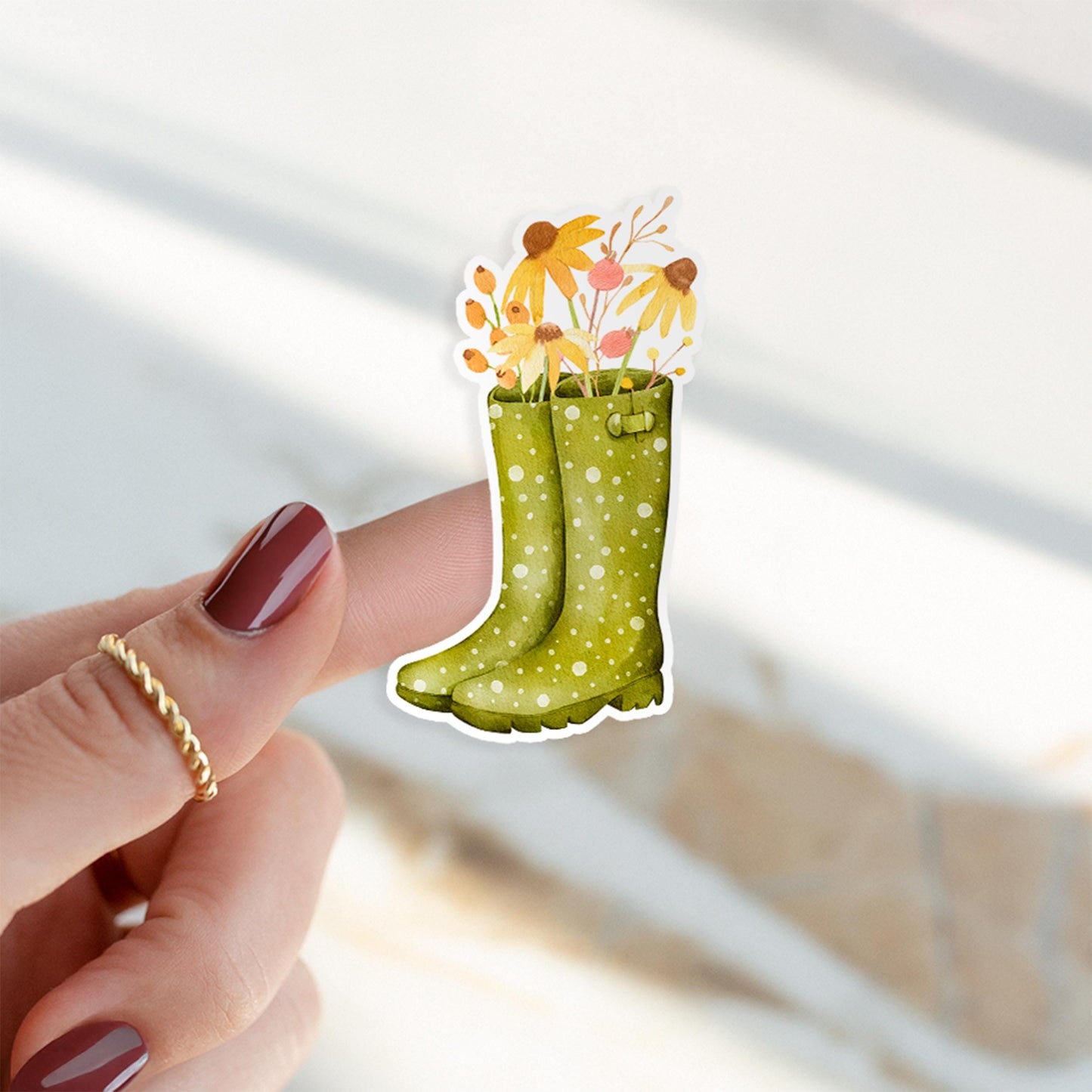 Auf einem Finger ist ein Sticker in Form eines Gummistiefels zu sehen, der den handgemalten Herbstblumen-Sticker repräsentiert, inspiriert von der Natur.