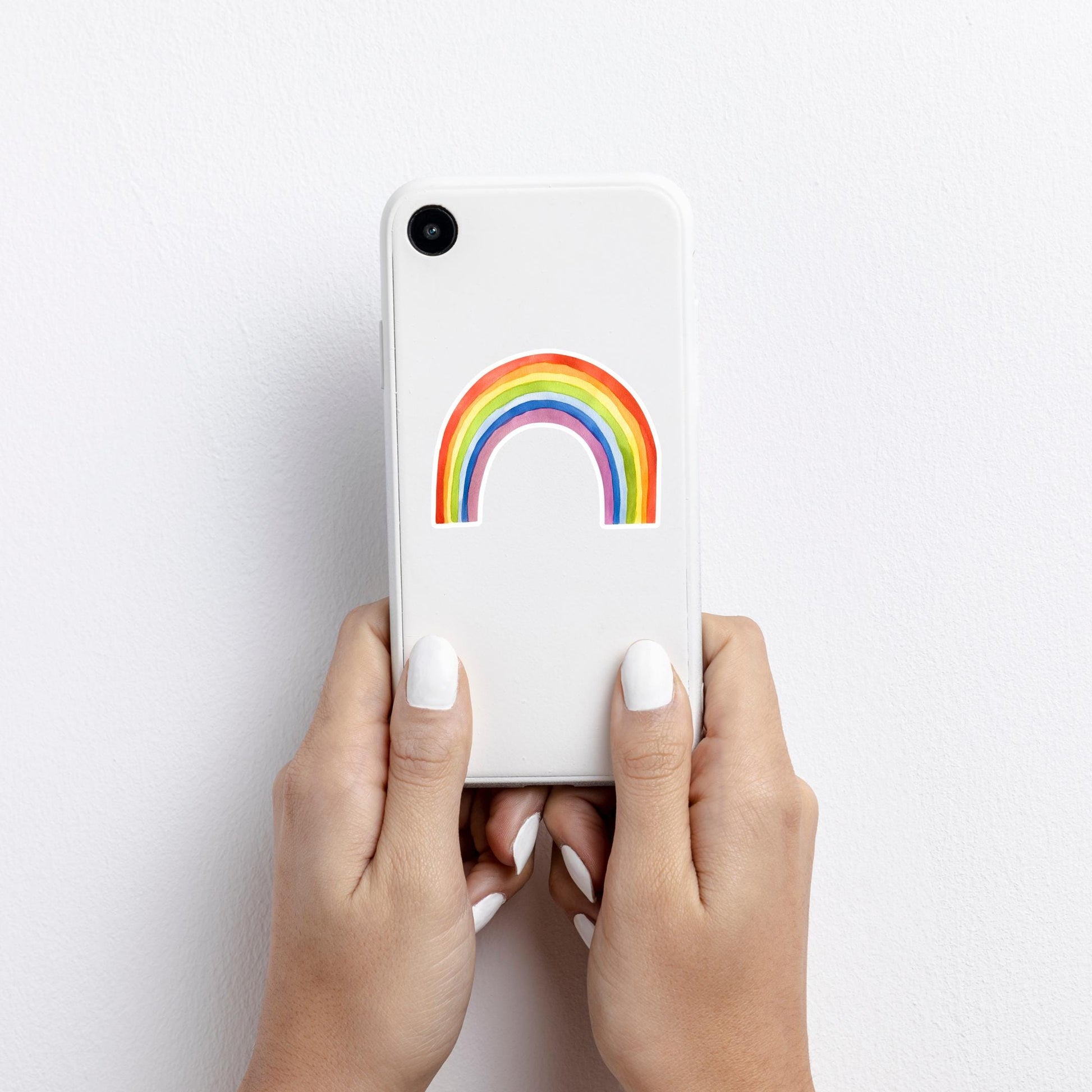 Hände halten ein kleines weißes Smartphone mit dem Sticker Regenbogen, einem handgemalten Vinyl-Aufkleber, der positive Energie ausstrahlt, spritzfest und langlebig.