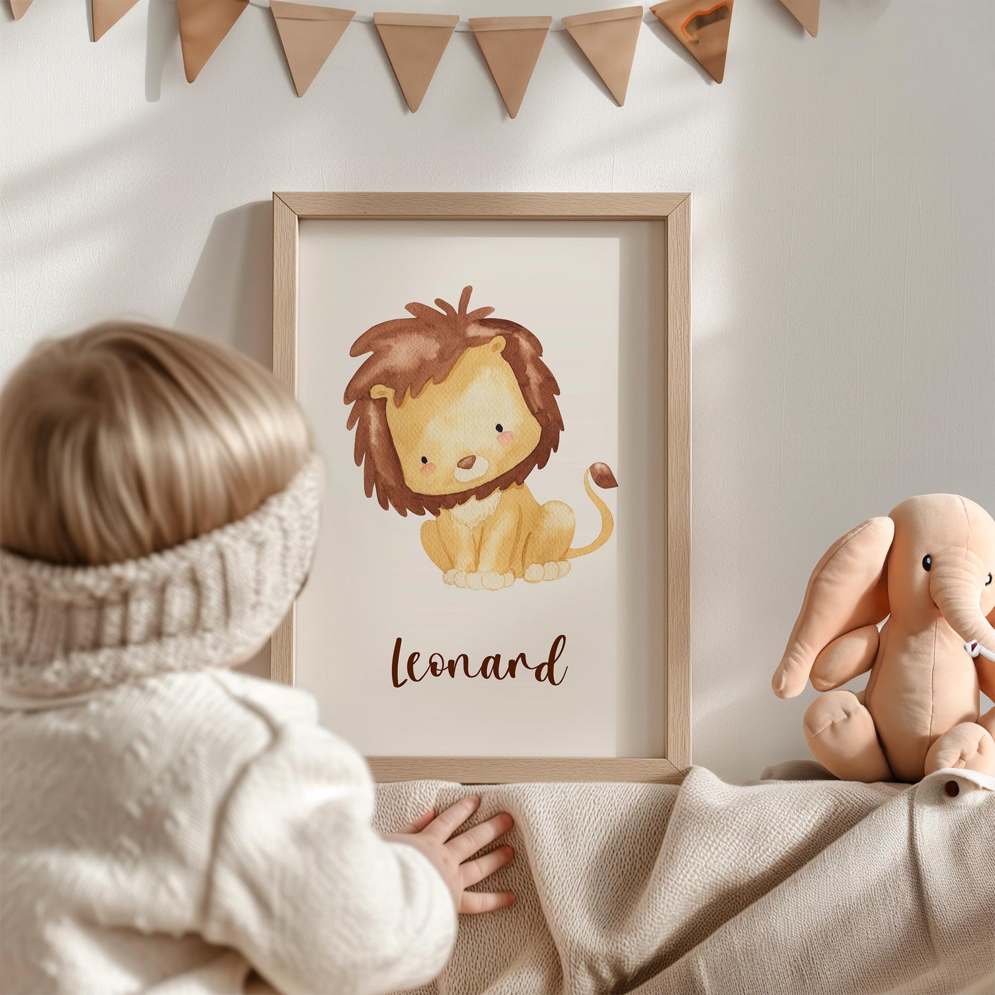 Kleinkind betrachtet Geburtsposter Löwe - personalisiert mit Leonard, daneben ein Plüschelefant. Warmes, neutrales Kinderzimmer-Dekor mit Wimpelkette darüber.