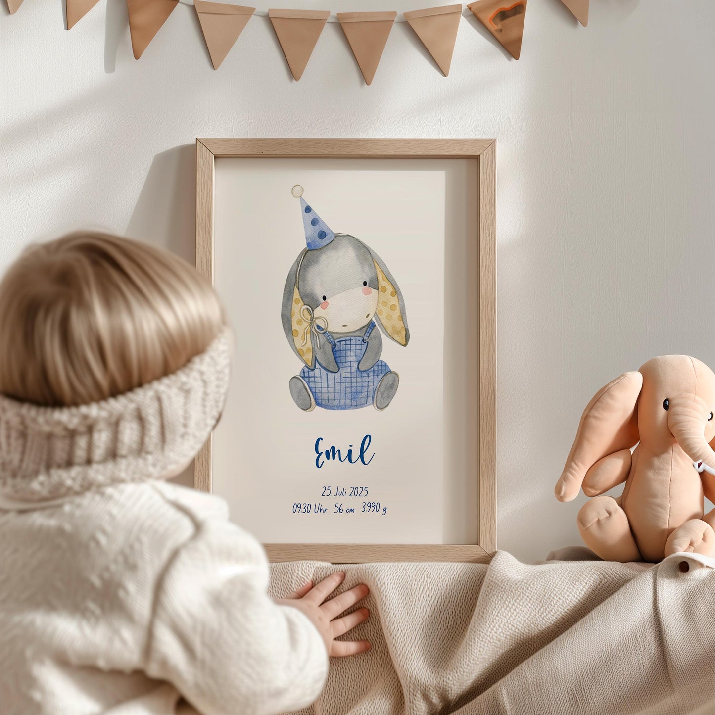 Geburtsposter Esel personalisiert im Holzrahmen zeigt einen grauen Aquarell-Hasen mit Partyhut; daneben ein Elefanten-Plüschtier, Kind betrachtet neugierig das Bild.