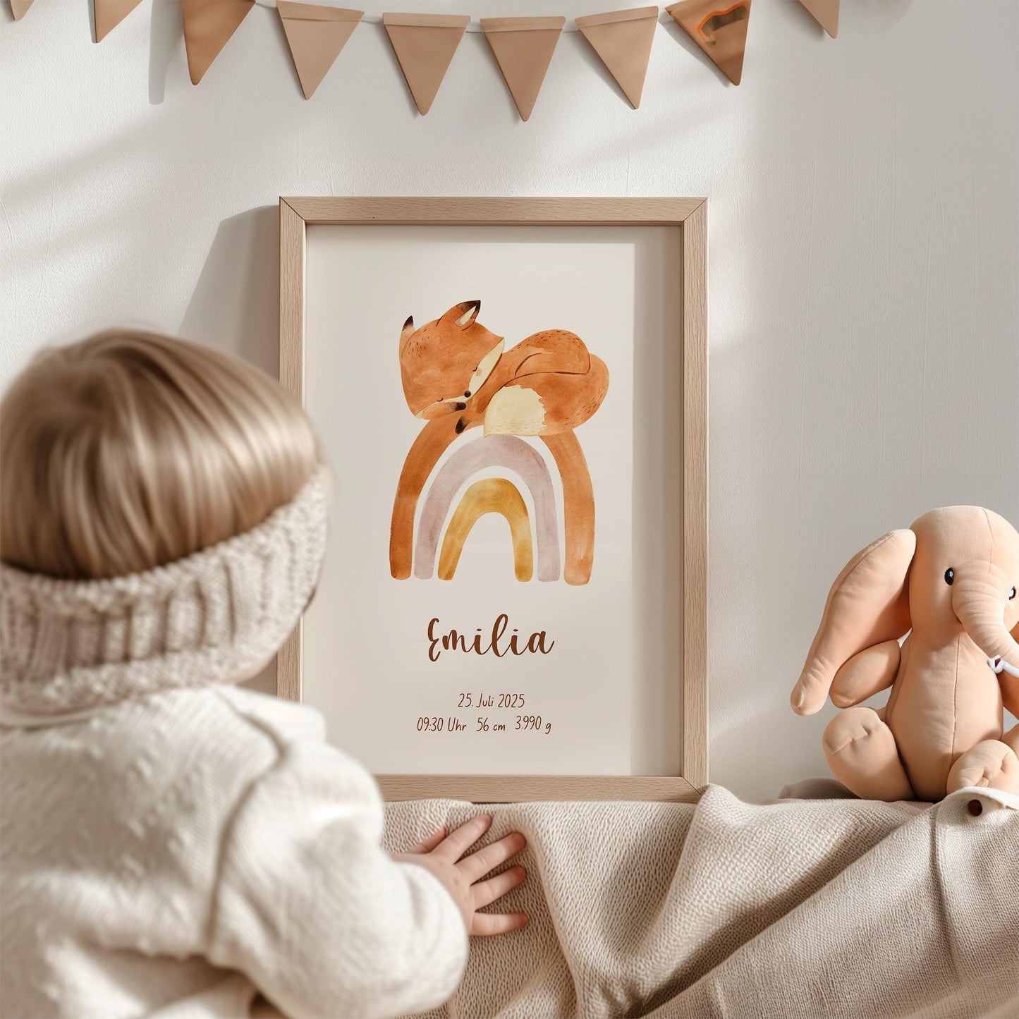 Kleinkind betrachtet ein Geburtsposter Fuchs auf Regenbogen personalisiert, mit individuellen Geburtsdaten, im Kinderzimmer. Daneben steht ein Plüschelefant auf einer Decke.