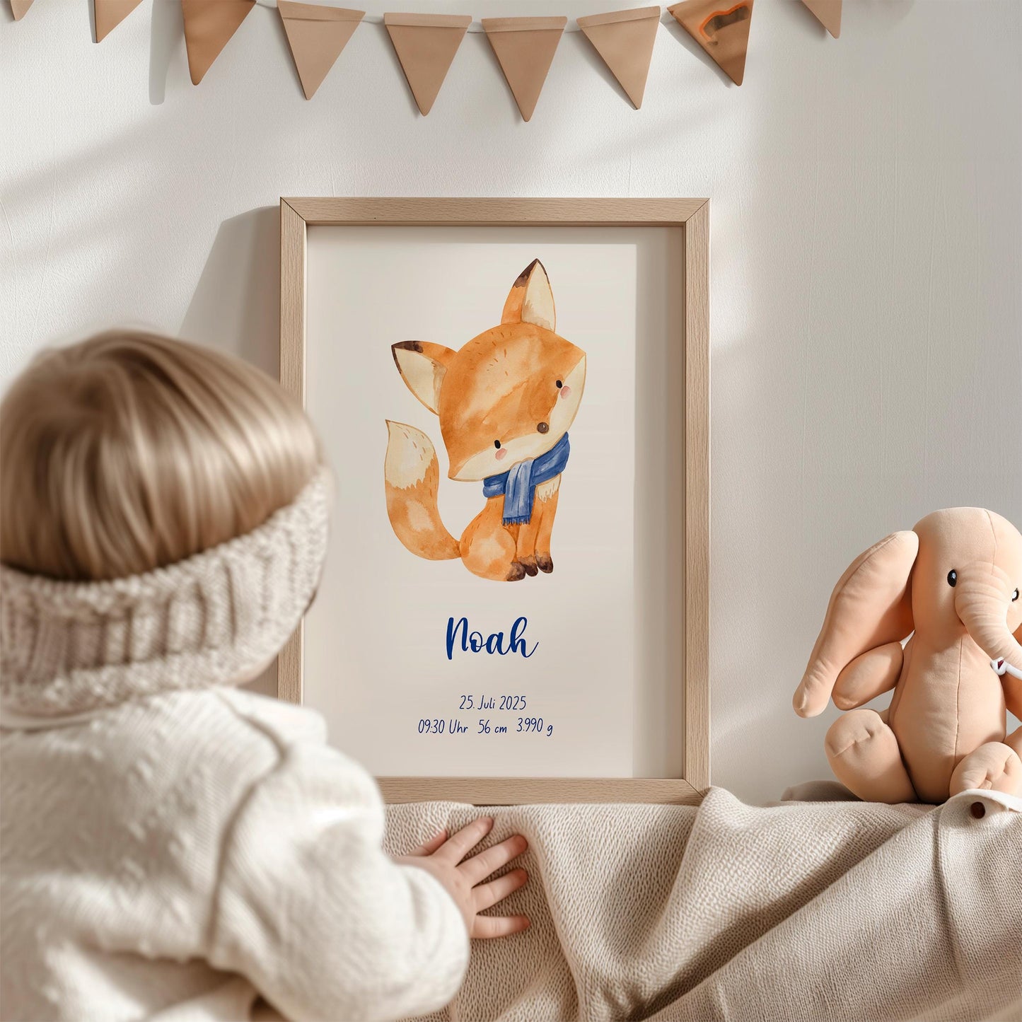 Geburtsposter Fuchs personalisiert: Kind betrachtet gerahmtes Poster mit Fuchsillustration, Name Noah, Geburtsdaten; daneben Plüschelefant, oben Papiertgirlande.