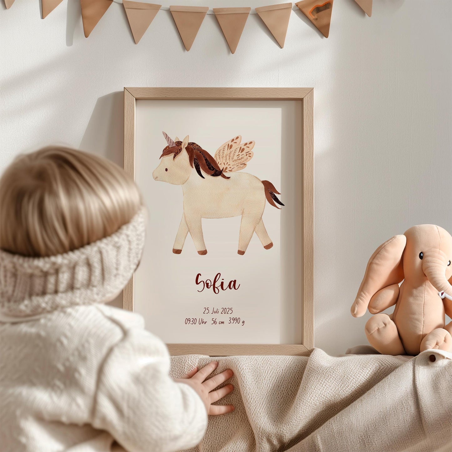 Kleinkind betrachtet Geburtsposter Einhorn - personalisiert, mit Namen und Geburtsdaten Sofia. Daneben ein Plüschelefant auf einer Decke.