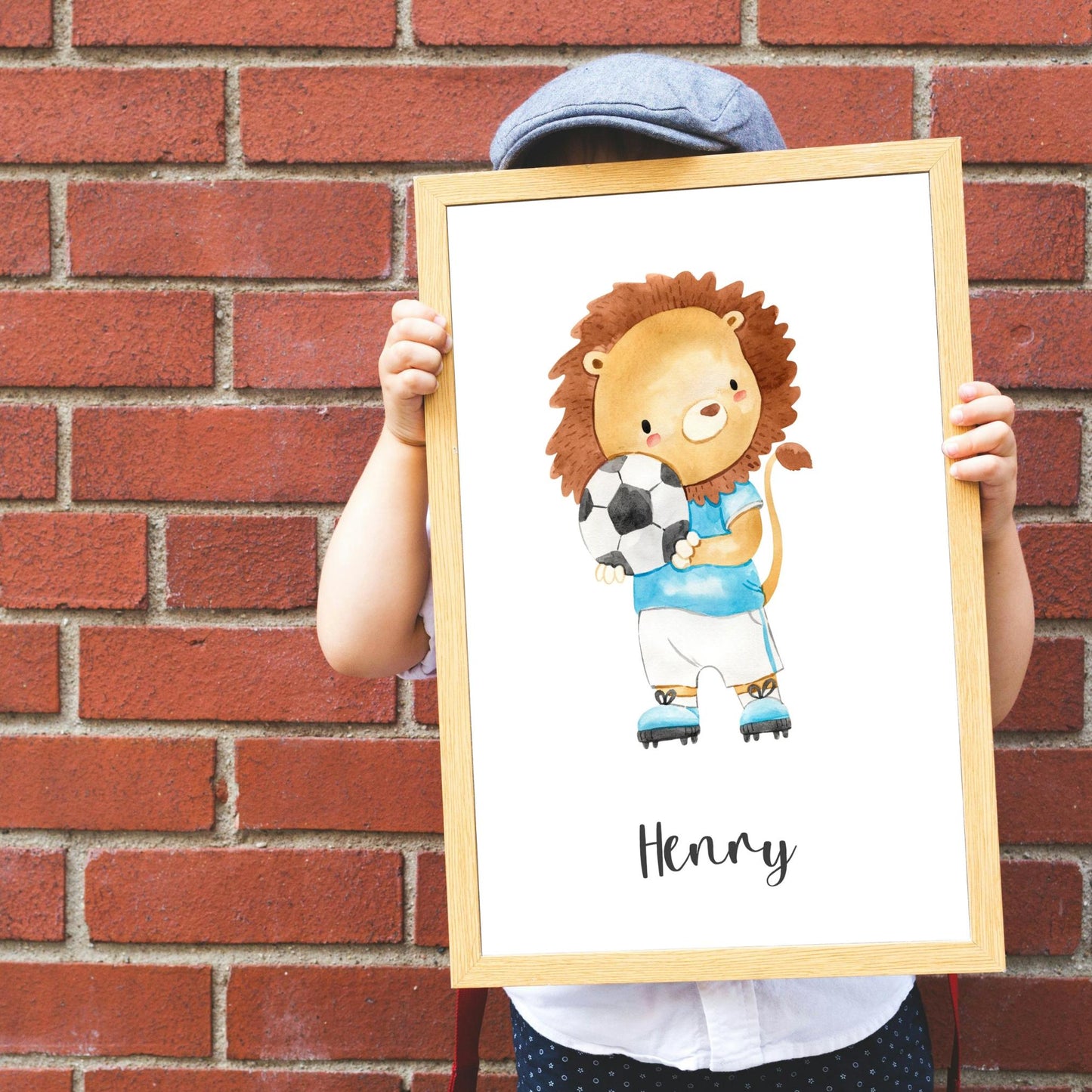 Kind hält Namensposter Fußball Löwe - personalisiert: Aquarell-Löwe im Fußballtrikot, Name Henry darunter, auf hochwertigem Naturpapier, ideal für Kinderzimmer-Deko.