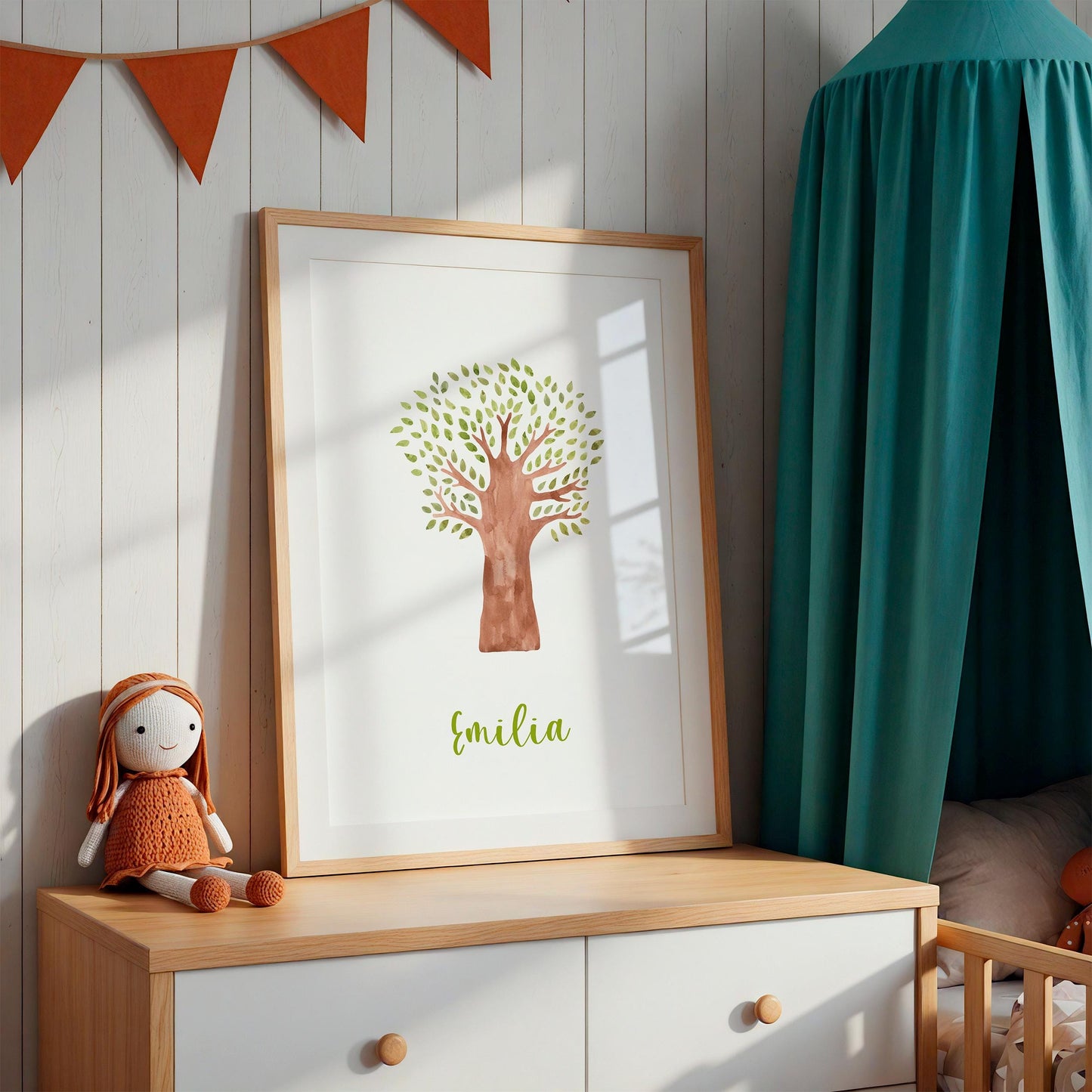 Geburtsposter Baum personalisiert: Holzrahmen mit Aquarellbaum und Emilia darauf, auf heller Kommode, daneben handgestrickte Puppe, orange Wimpelkette darüber.