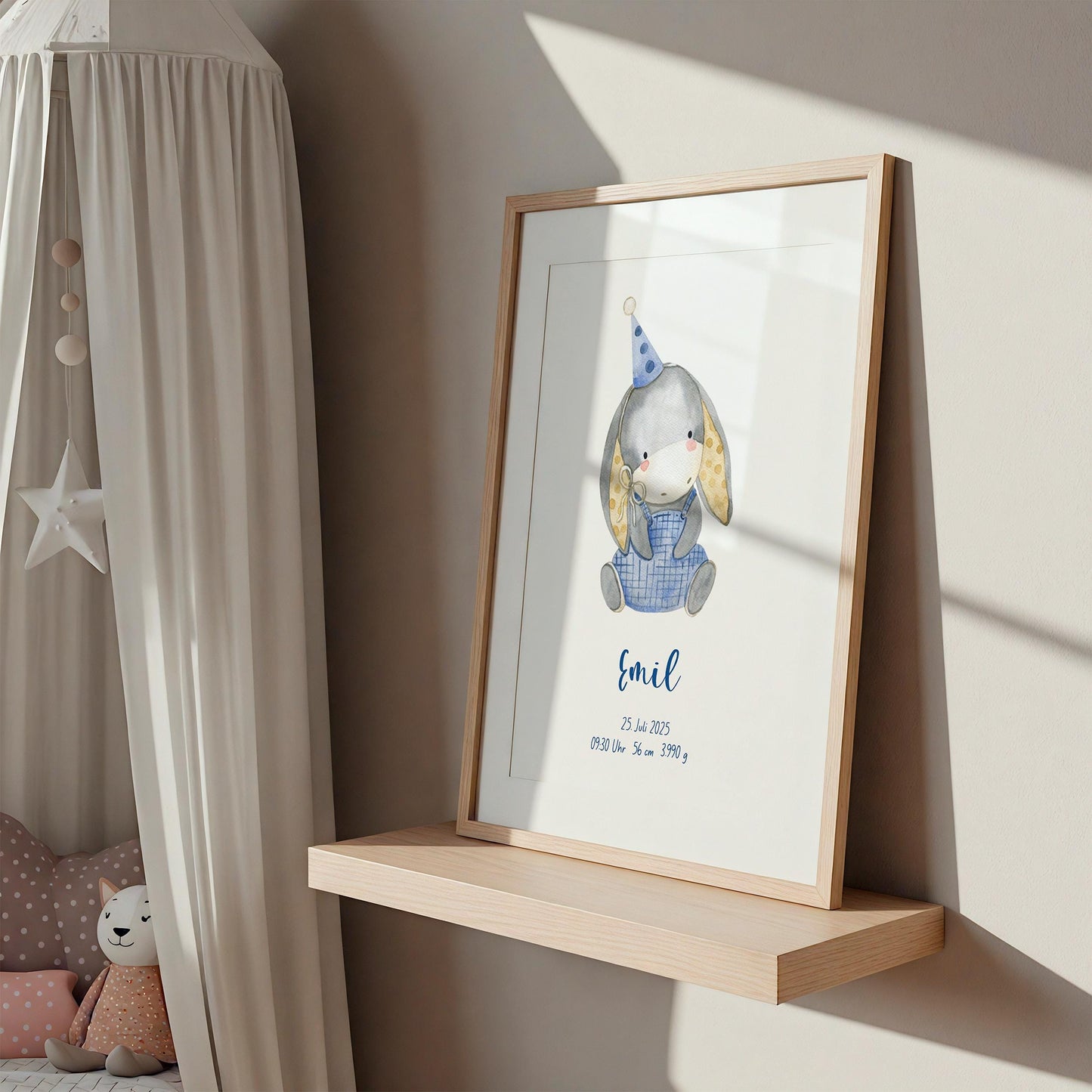 Geburtsposter Esel personalisiert auf einem Regal, zeigt einen Hasen mit Partyhut und Emil's Geburtsdaten. Daneben eine gemütliche Ecke mit Stoffkatze und Kissen.