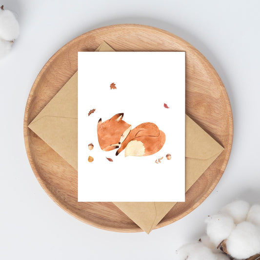 Runde Holzschale mit Karte Fuchs & Herbstlaub A6 auf einem Umschlag, umgeben von Baumwollzweigen. Aquarell-Fuchs in Herbstblättern und Eicheln, auf hochwertigem Naturpapier.