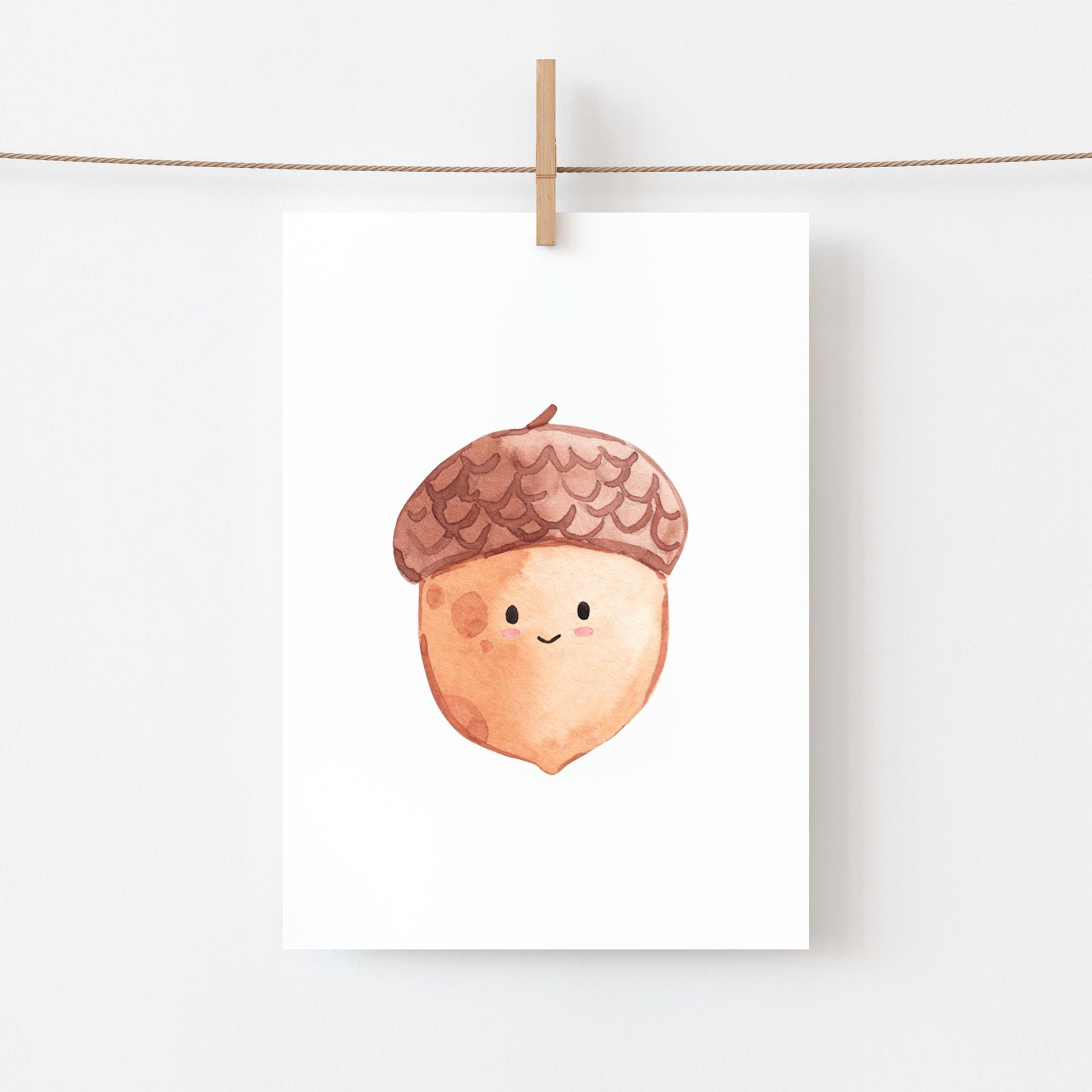 Postkarte Karte Eichel A6 zeigt eine lächelnde Eichel-Illustration, befestigt mit Holzklammer an einem Faden. Ideal als Grußkarte oder herbstliche Dekoration.