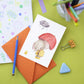 Karte Elefant und Entchen A6: Elefant in gelbem Regenmantel mit einem Entchen, gedruckt auf stabilem 300g Naturpapier. Karte auf Basteltisch für Kinder.