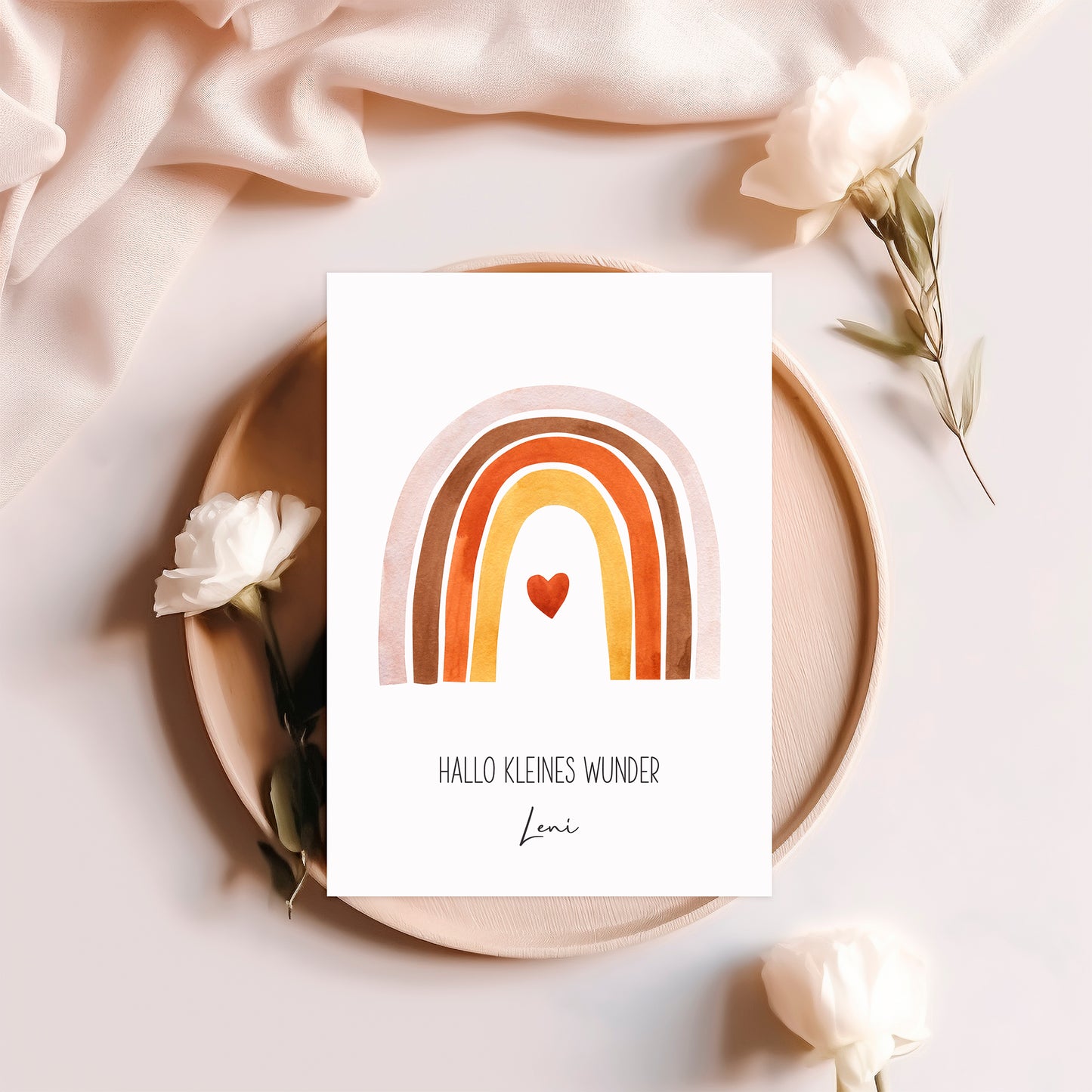 Personalisierte Geburtskarte Regenbogen & Herz A6 mit handgemaltem Regenbogen und Herz. Auf hellem Holztablett platziert, umgeben von weißen Rosen und Stoff.