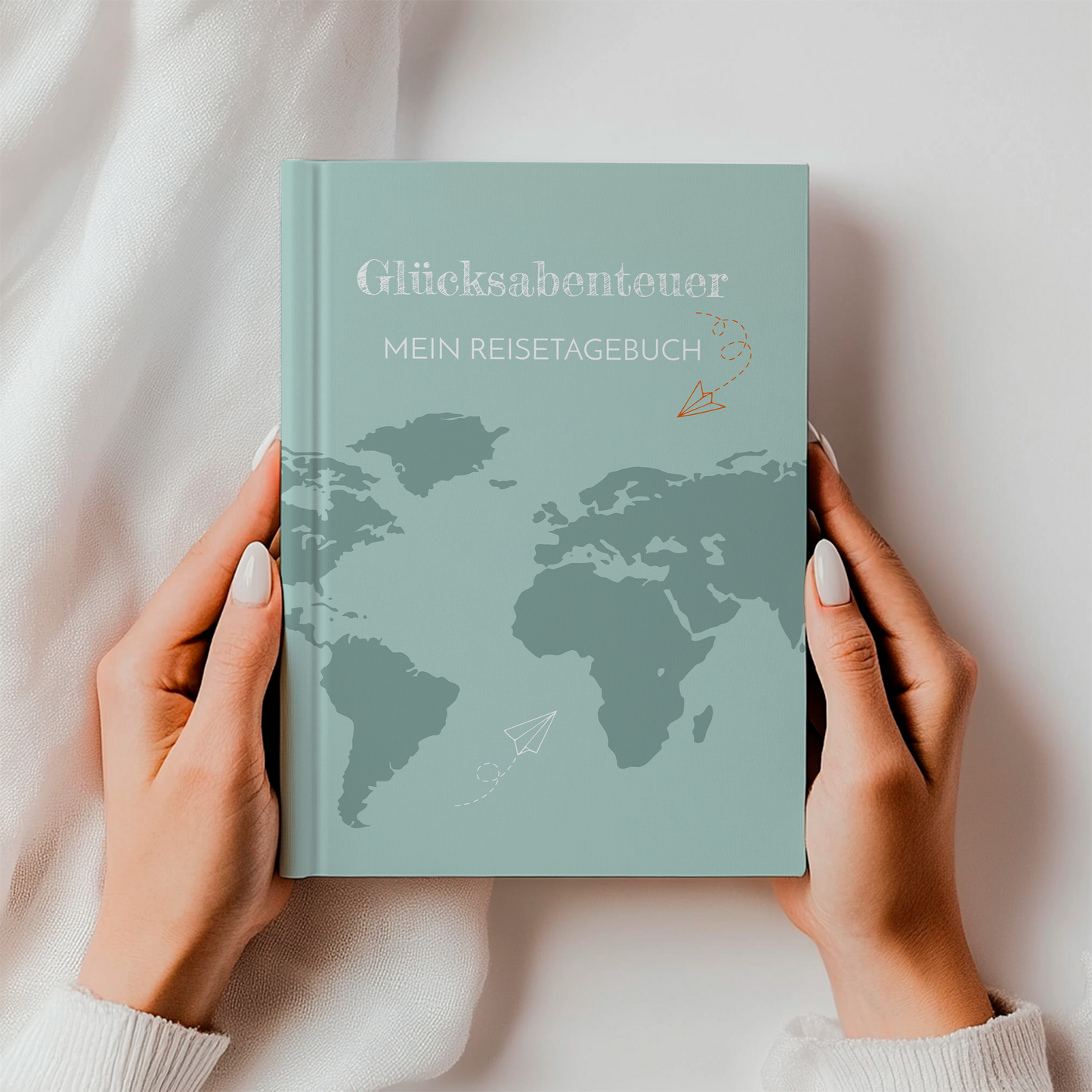 Person hält Reisetagebuch Glücksabenteuer A5 Hardcover: Notizbuch mit einer Weltkarte und Papierfliegern auf dem Cover, ideal zum Planen und Festhalten von Reiseerinnerungen.