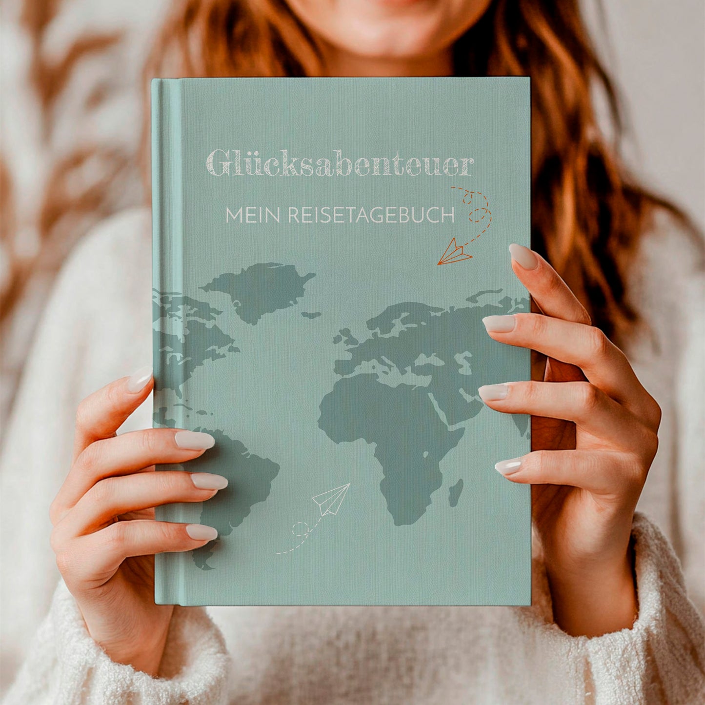 Person hält Reisetagebuch Glücksabenteuer A5 Hardcover: Notizbuch mit einer Weltkarte und Papierfliegern auf dem Cover, ideal zum Planen und Festhalten von Reiseerinnerungen.