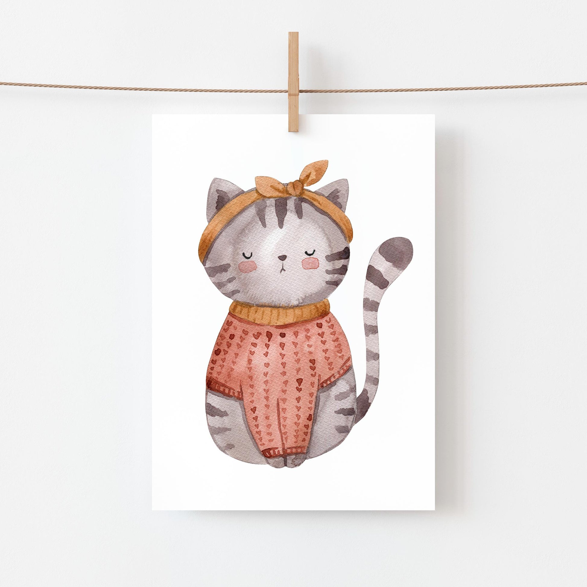 Karte Katze Vintage A6: eine Aquarellillustration einer Katze im Pullover mit Schleife, ideal für Glückwünsche oder als Geschenk, auf hochwertigem Naturpapier. Hängt an einer Wäscheleine.