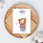 Postkarte Karte Bär im Schnee A6 mit Teddybär-Aquarell, der eine im Schnee. Auf einem Holzbrett mit Umschlag platziert.