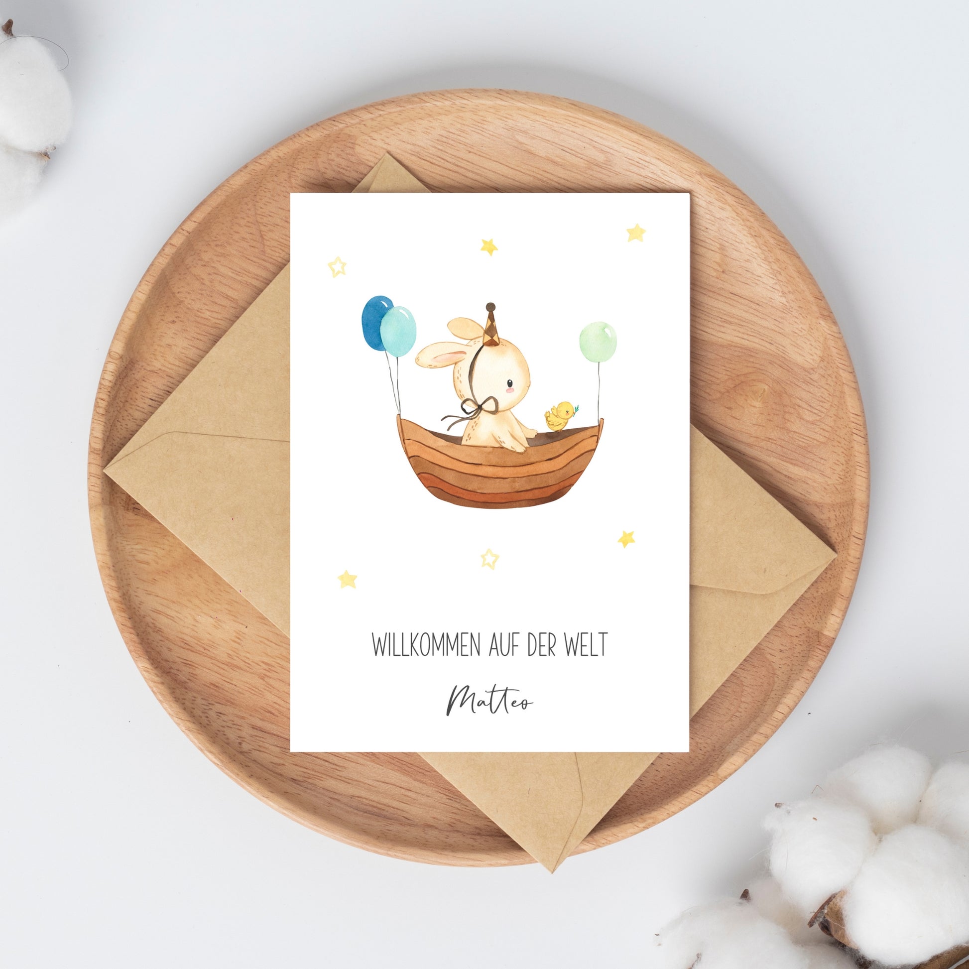 Personalisierte Geburtskarte Hase & Luftschiff A6 auf Holzplatte, zeigt Hase im Boot mit Ballons, neben Küken, mit WILLKOMMEN AUF DER WELT Matteo Schriftzug.