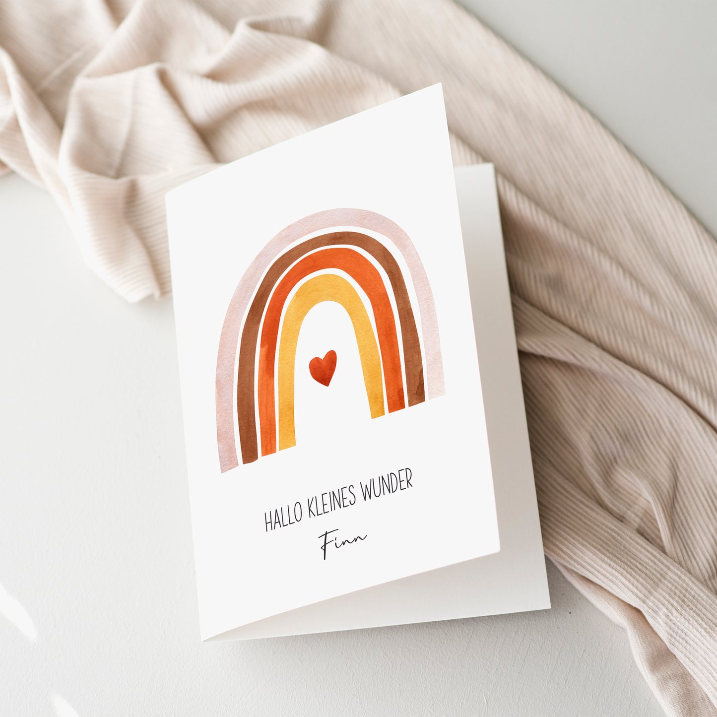 Personalisierte Geburtskarte Regenbogen & Herz A6 auf beigem Stoff, handgemalt mit Namen Finn und Hallo kleines Wunder Text, im Boho-Stil.