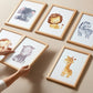 Posterset Safari: Sechs Aquarelldrucke mit Elefant, Löwe, Zebra, Affe, Hippo, Giraffe in Holzrahmen, ideal für Kinderzimmer. Hände arrangieren zwei Bilder.