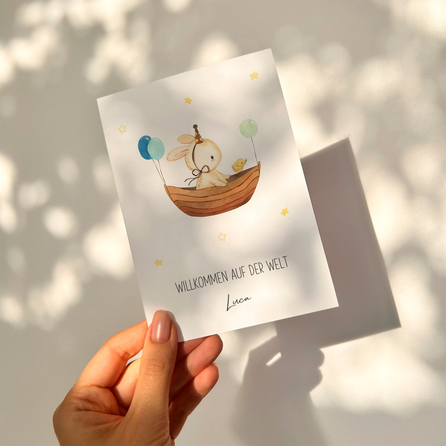 Personalisierte Geburtskarte Hase & Luftschiff A6 zeigt einen Hasen im Boot mit Ballons und Küken, unter dem Text Willkommen auf der Welt, Luca.