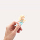 Hand hält Sticker Meerjungfrau blond, cartoonartig, aus hochwertigem Vinyl, ideal für Dekorationen. Spritzfest und langlebig, perfekt für kreative Anwendungen.