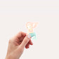 Hand hält den Sticker Meerjungfrau rosa, einen handgefertigten, langlebigen Vinyl-Aufkleber in Pastelltönen. Ideal für Dekoration von Notizbüchern, Laptops oder Handyhüllen.