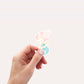 Hand hält Sticker Meerjungfrau pink, ein handgemalter Vinyl-Aufkleber in Pastelltönen, ideal für Bullet Journals oder Laptops, spritzfest und langlebig.