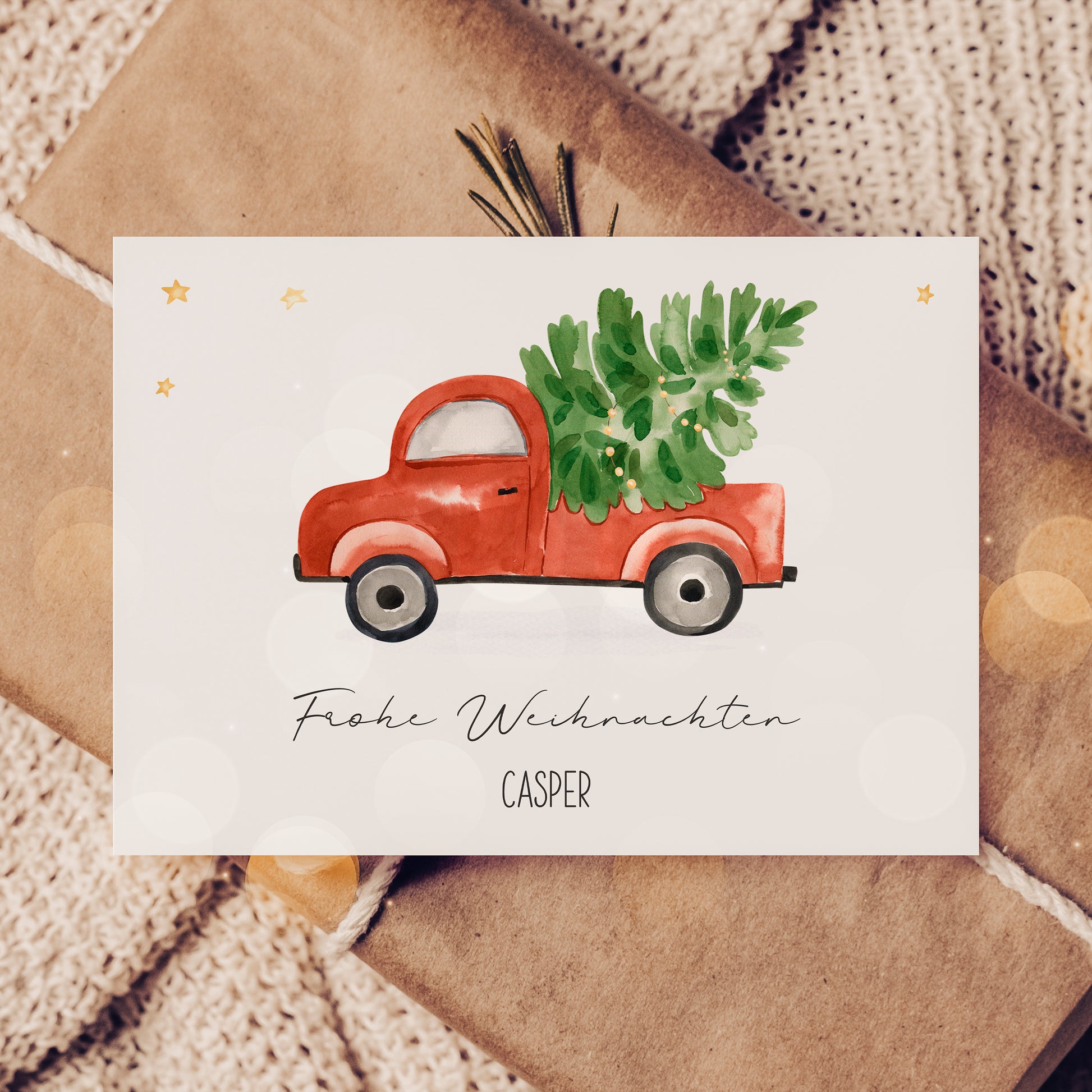 Personalisierte Weihnachtskarte Auto & Baum A6 auf Geschenk, zeigt Aquarell eines roten Trucks mit Tannenbaum, umgeben von goldenen Sternen und Frohe Weihnachten Text.